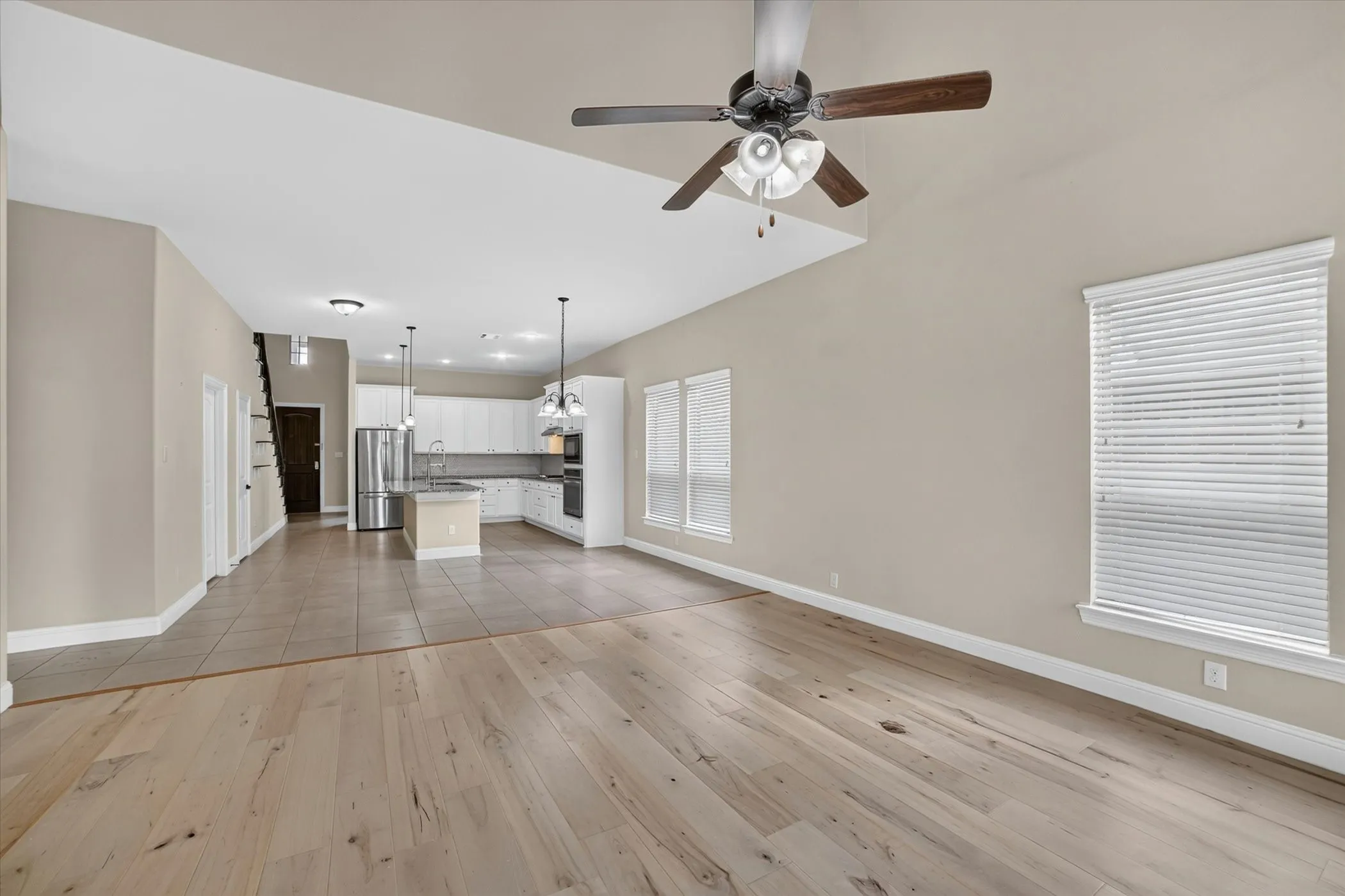 Vaulted ceiling living area featuring wood-finish flooring, a contemporary ceiling fan, and multiple windows with blinds