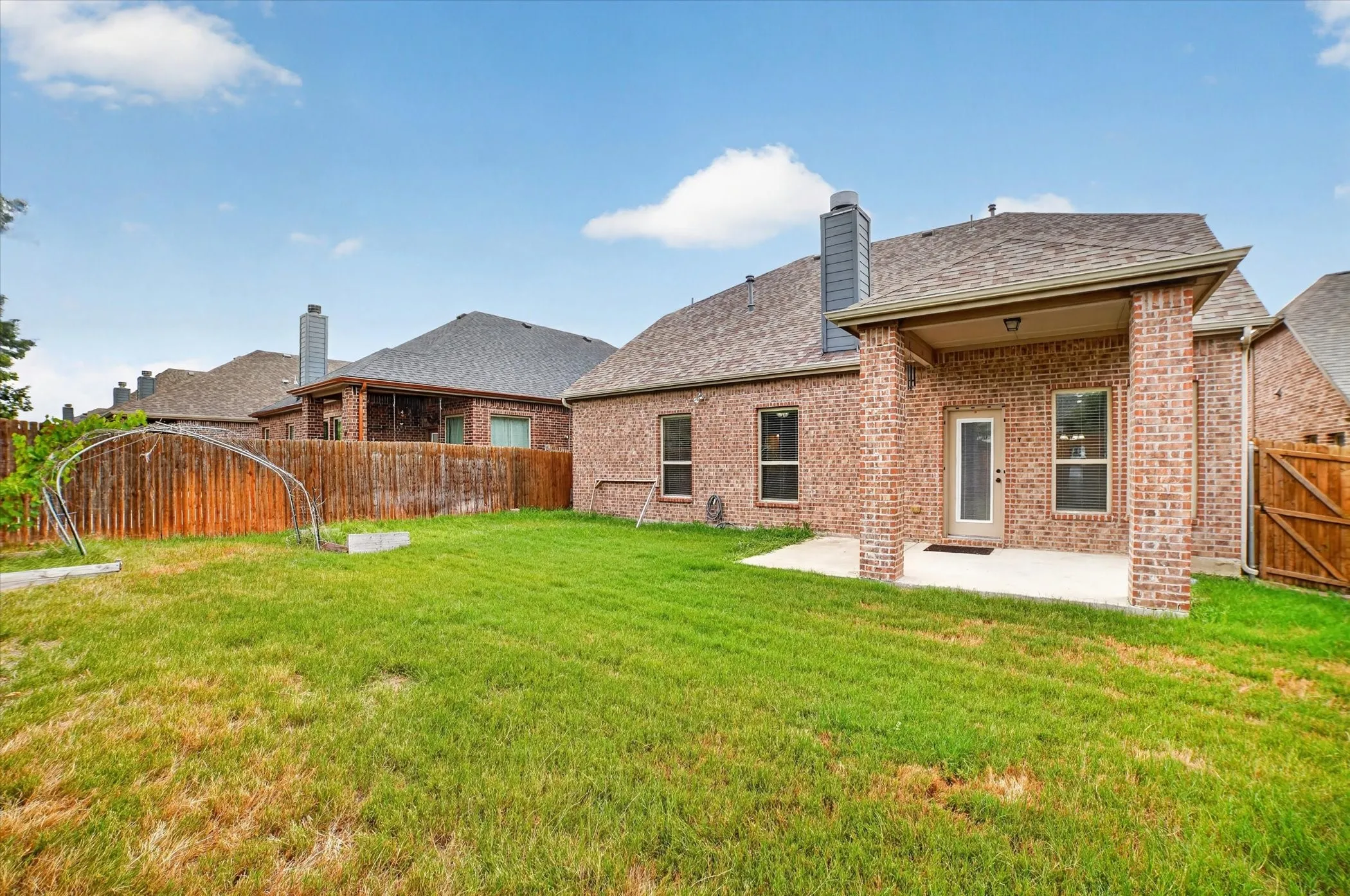 Expansive backyard featuring a brick exterior, covered patio, and a privacy fence
