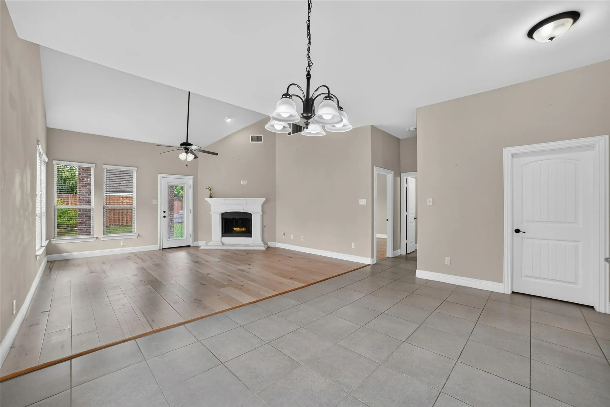 Vaulted ceiling great room featuring a decorative fireplace, wood-finish flooring, and large windows