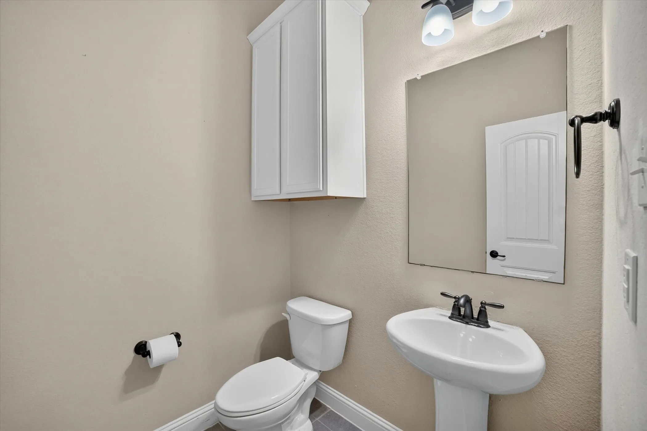 Pedestal sink with dark bronze fixtures, wall-mounted mirror, and overhead vanity lighting