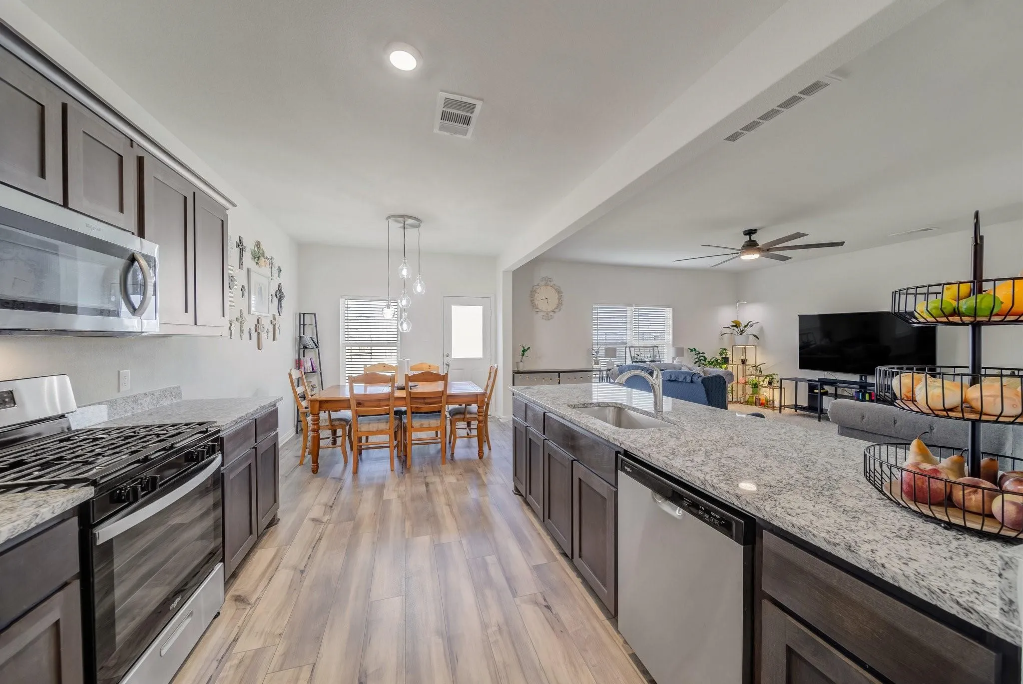 Open-concept kitchen featuring dark wood cabinetry, stainless steel appliances, granite countertops, and wood-finish flooring