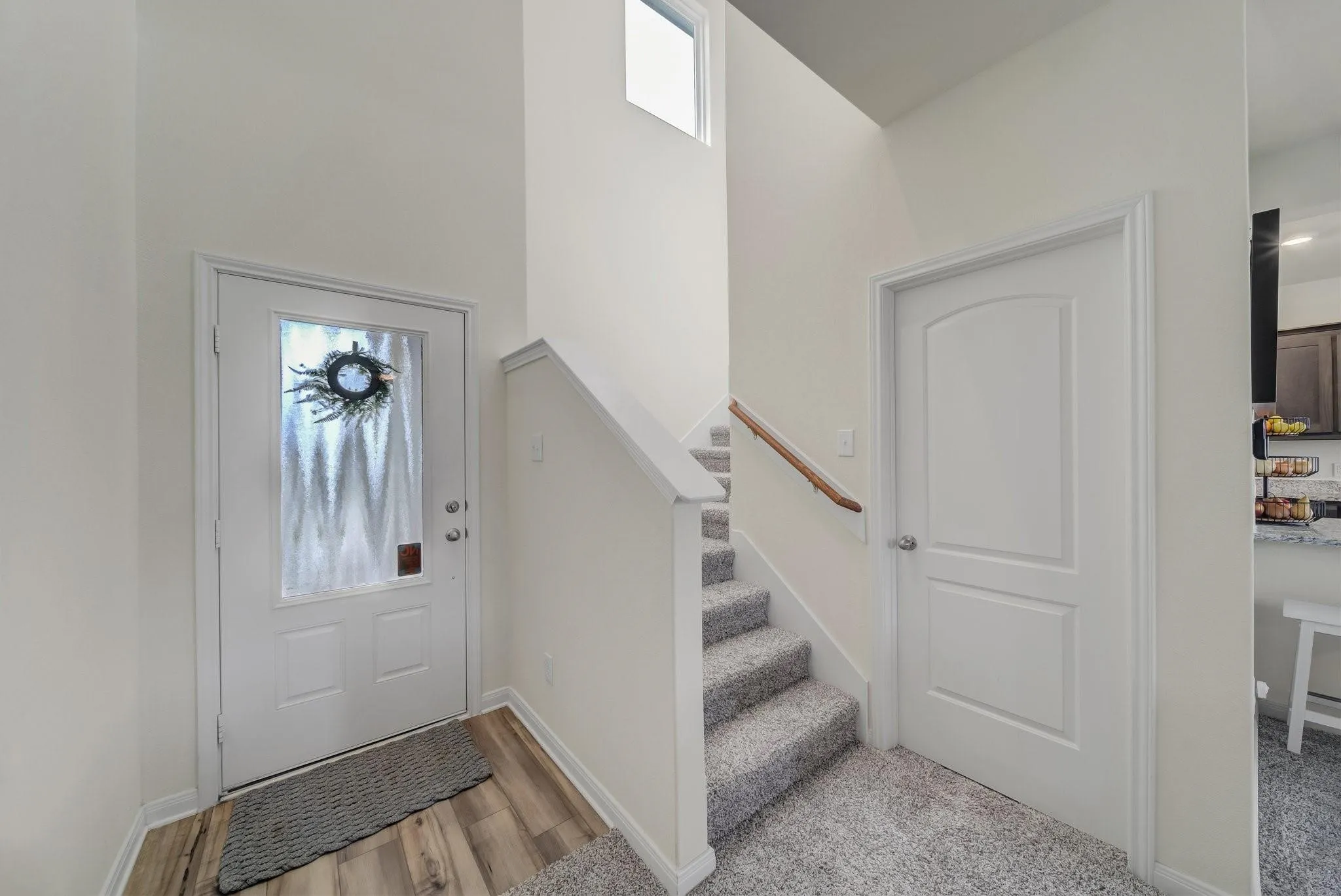 Entryway featuring a white door with an opaque glass insert, wood-finish flooring, a carpeted staircase with a wood handrail, and high ceilings with a transom window