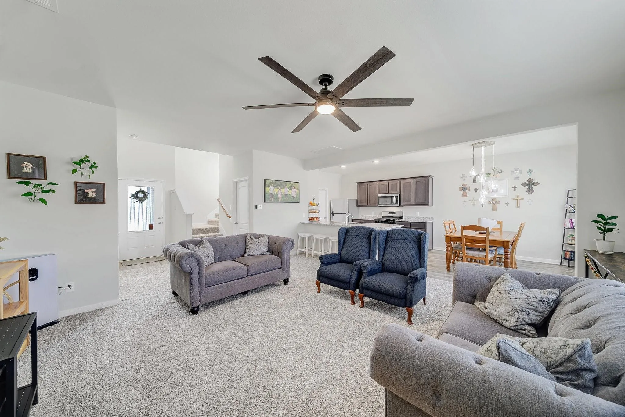 Bright open-concept living area with light carpeting, a contemporary ceiling fan, and white painted walls