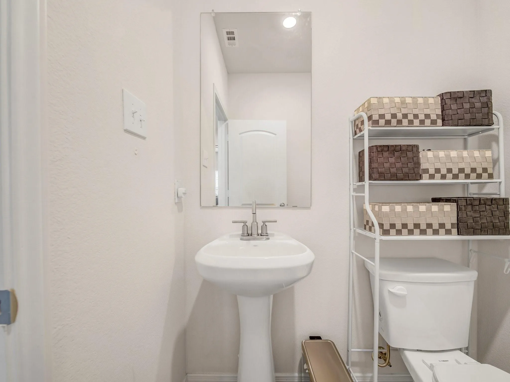 Pedestal sink with chrome faucet, complemented by a wall-mounted rectangular mirror