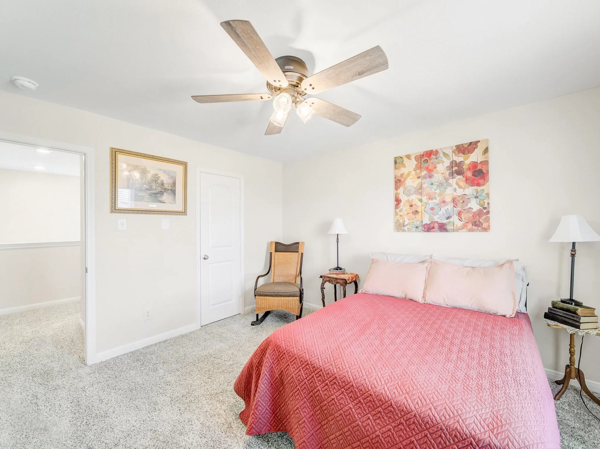 Bright bedroom featuring neutral wall tones, textured carpeting, a paddle fan with integrated lighting, and a white interior door