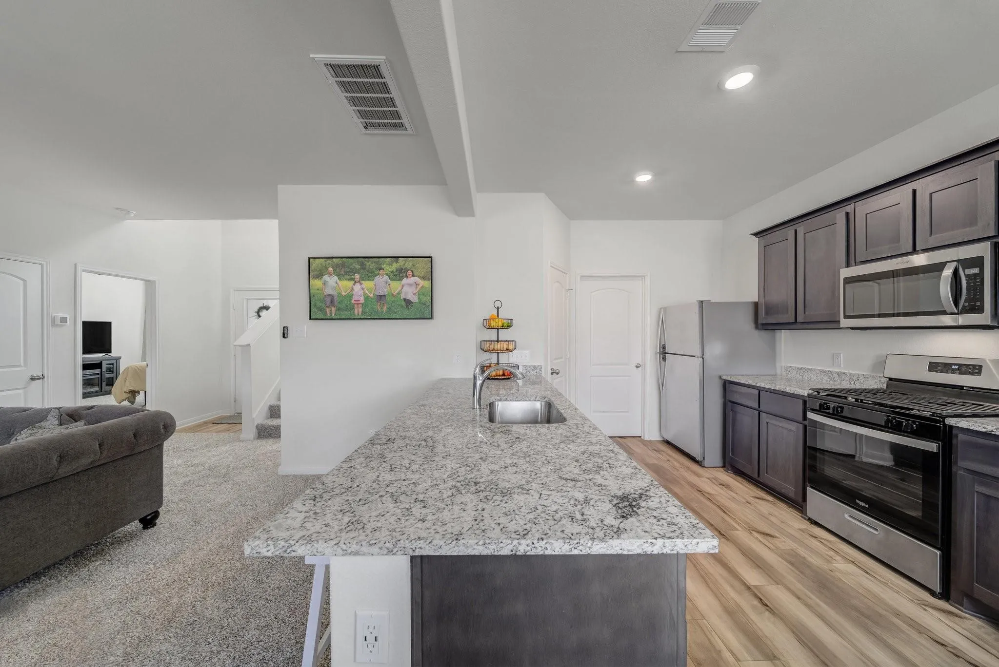 Open-concept kitchen featuring an island with an undermount sink, granite countertops, wood-finish flooring, and dark cabinetry