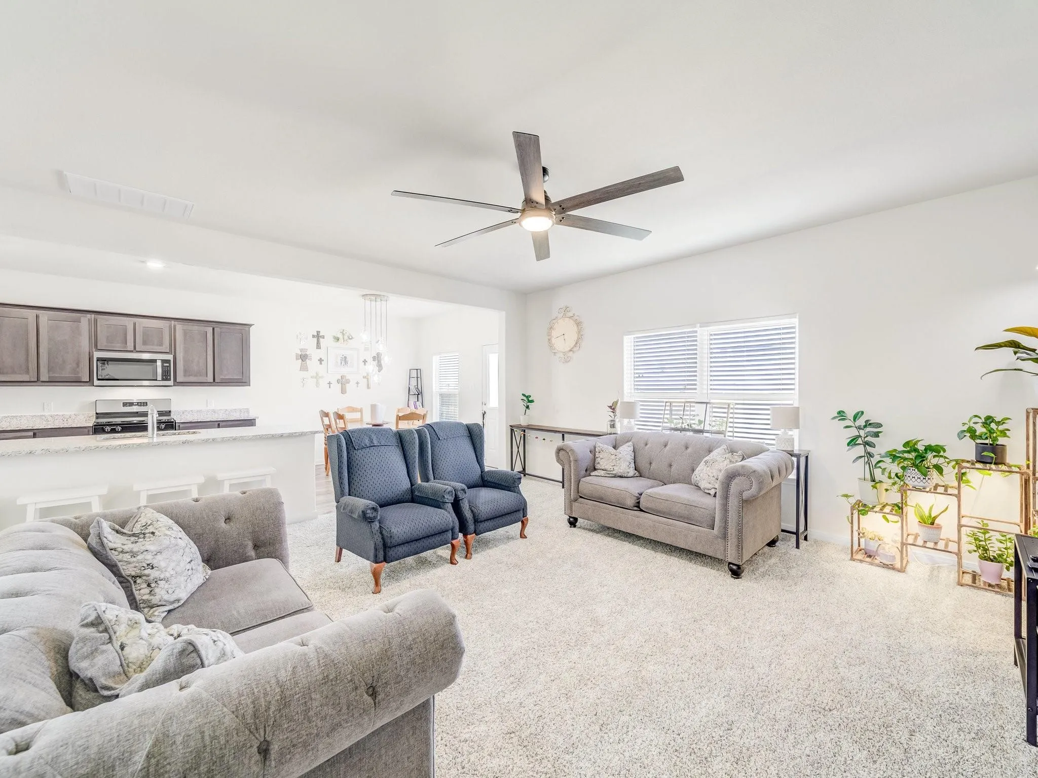 Open-concept living space featuring light-toned carpeting, a ceiling fan, and abundant natural light from horizontal windows