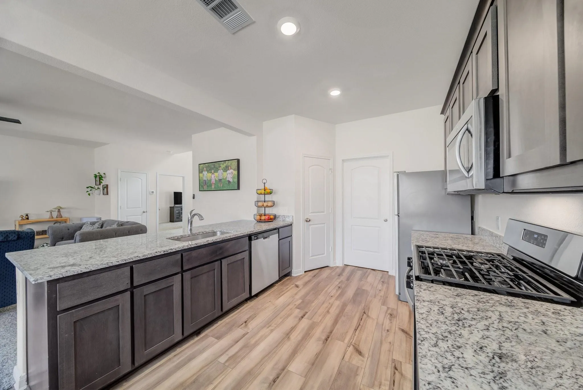 Modern kitchen featuring light wood-finish flooring, dark cabinetry, and granite countertops