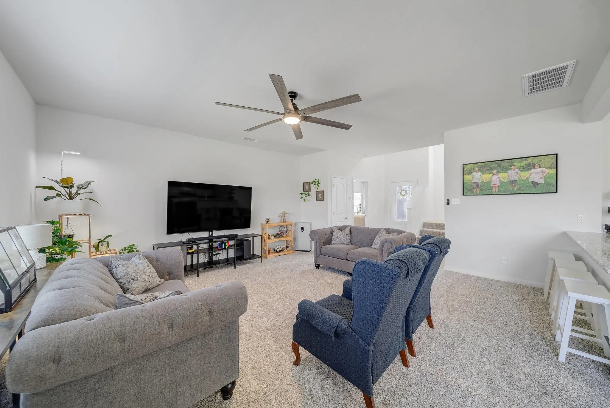 Spacious living area featuring light gray carpeting, a contemporary ceiling fan, and abundant natural light