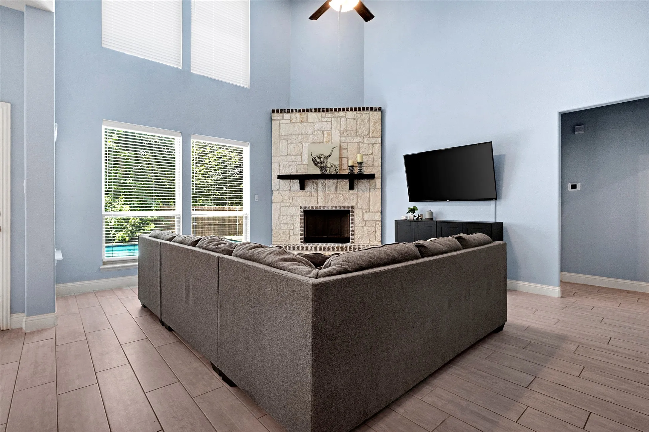 Spacious living area featuring a stone-clad fireplace with mantel, high ceilings, ceiling fan, and tile flooring