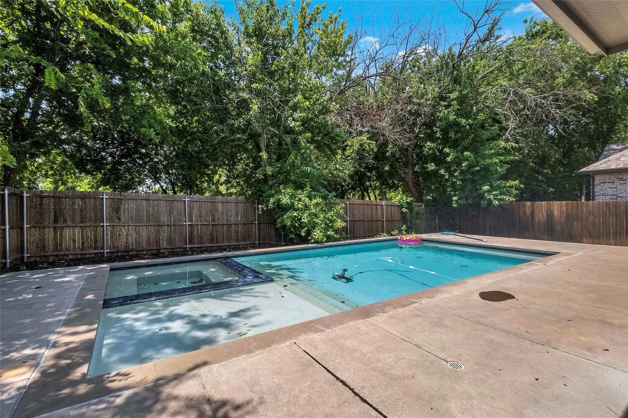 Outdoor swimming pool with integrated spa and surrounding concrete decking