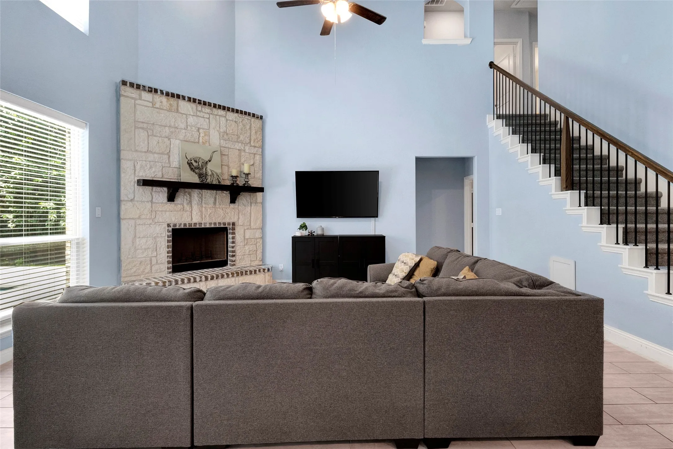 Spacious living area featuring a stone-clad fireplace with a dark wood mantel, high vaulted ceilings, and a ceiling fan