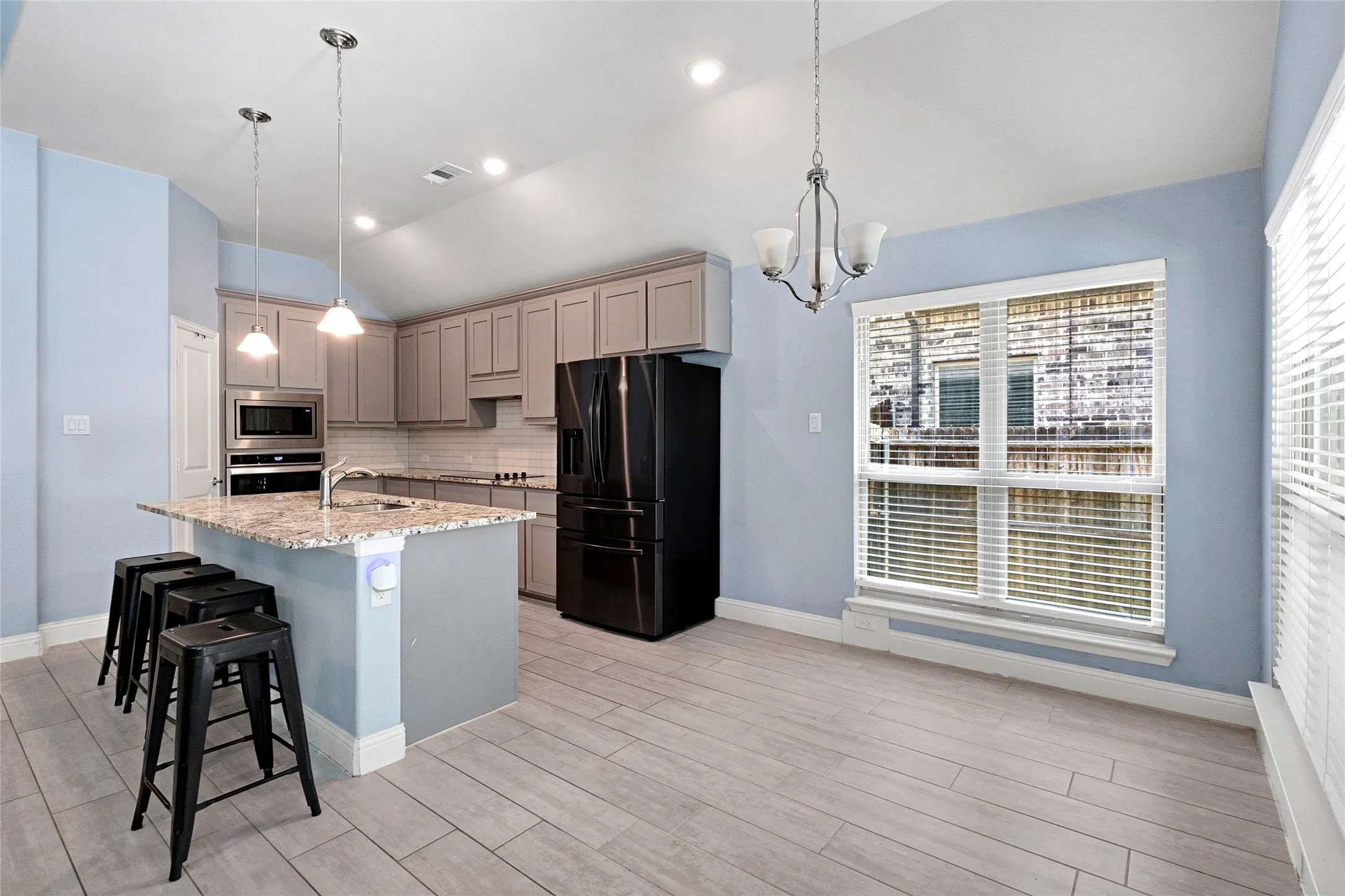 Open-concept kitchen and dining area featuring light wood-finish flooring, a kitchen island with stone countertop, gray cabinetry, and stainless steel appliances