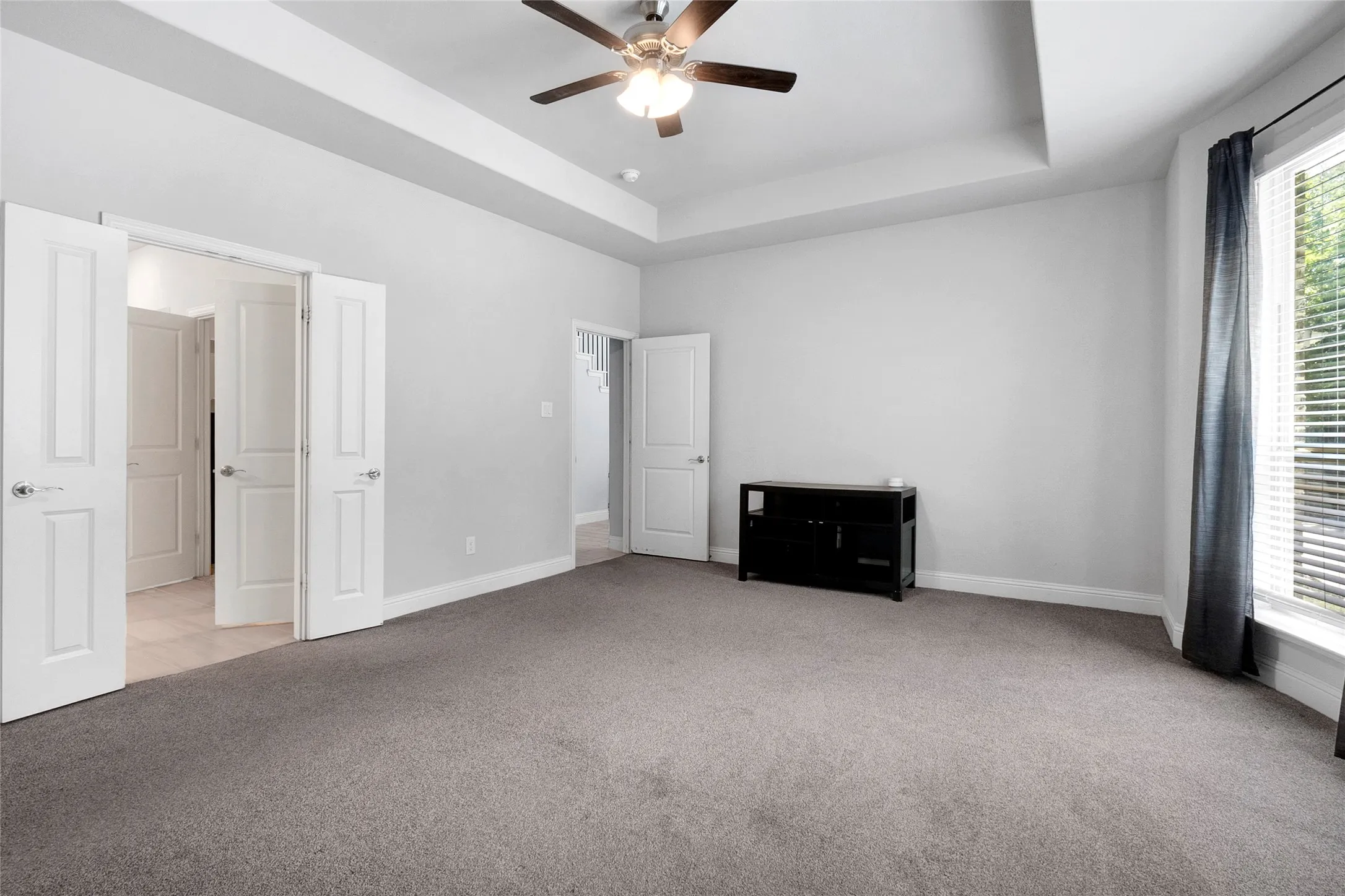 Spacious room featuring tray ceiling, ceiling fan, and light gray wall paint
