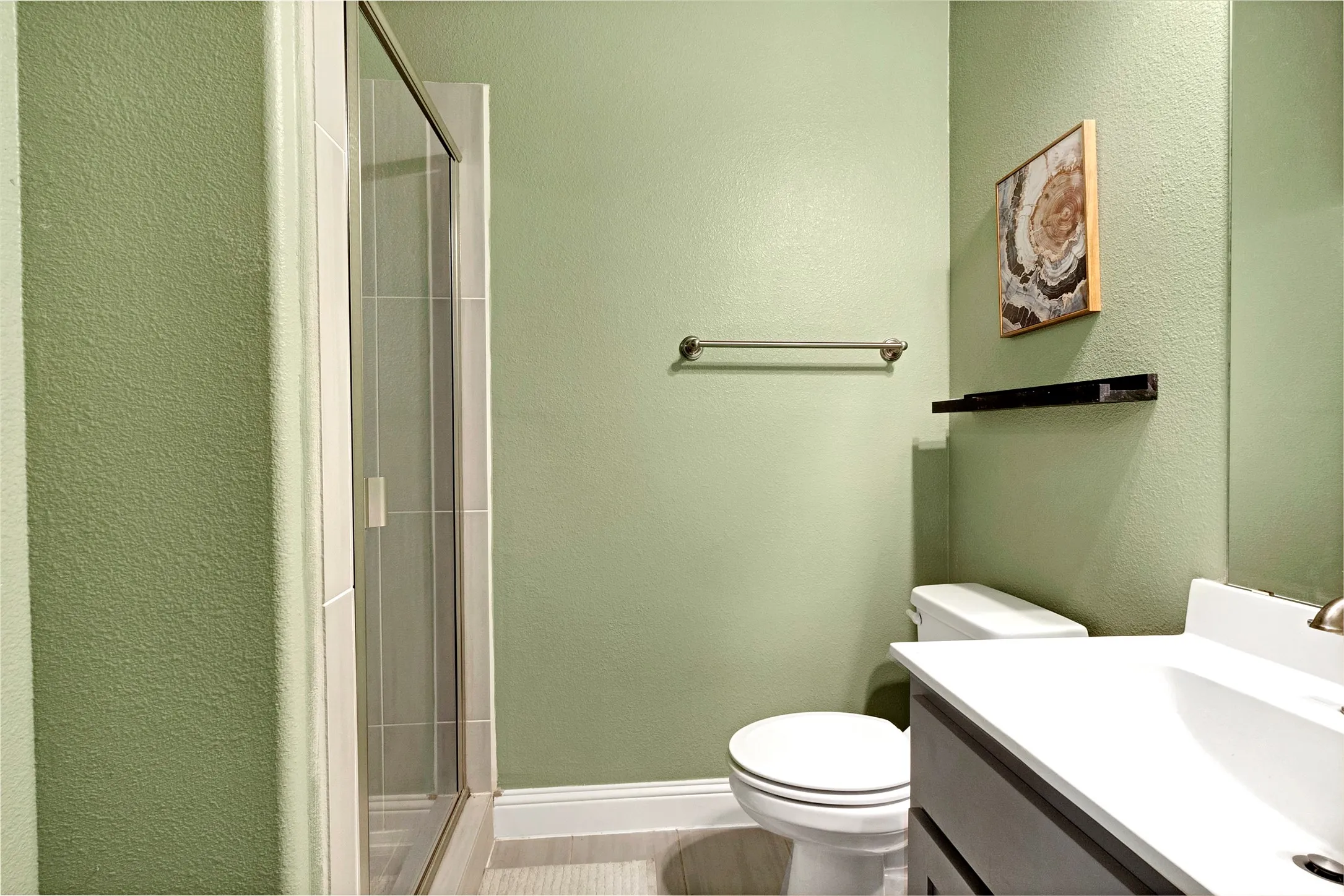 Bathroom featuring a glass-enclosed shower, white toilet, single-sink vanity with white countertop, and light green walls