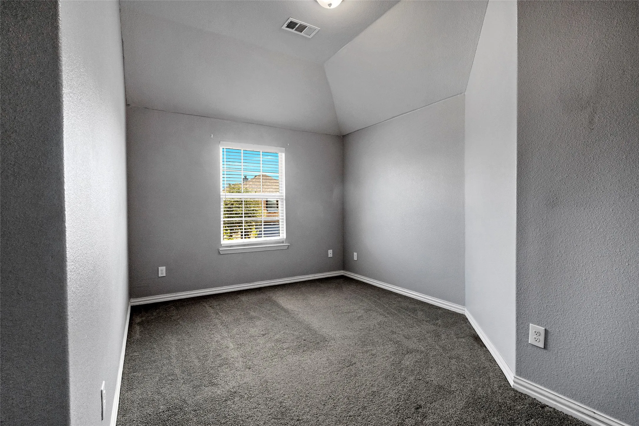 Grey carpeted room with a vaulted ceiling, a single window with blinds, and white baseboard trim
