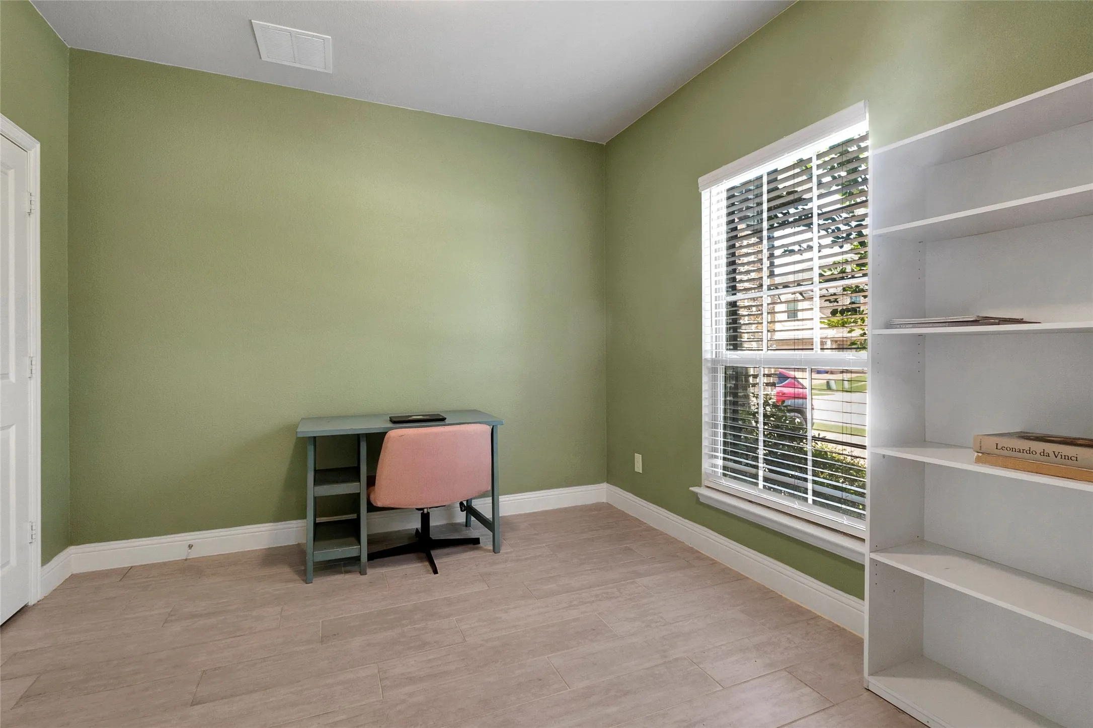 Room featuring wood-finish flooring, a double-hung window with blinds, and a built-in shelving unit