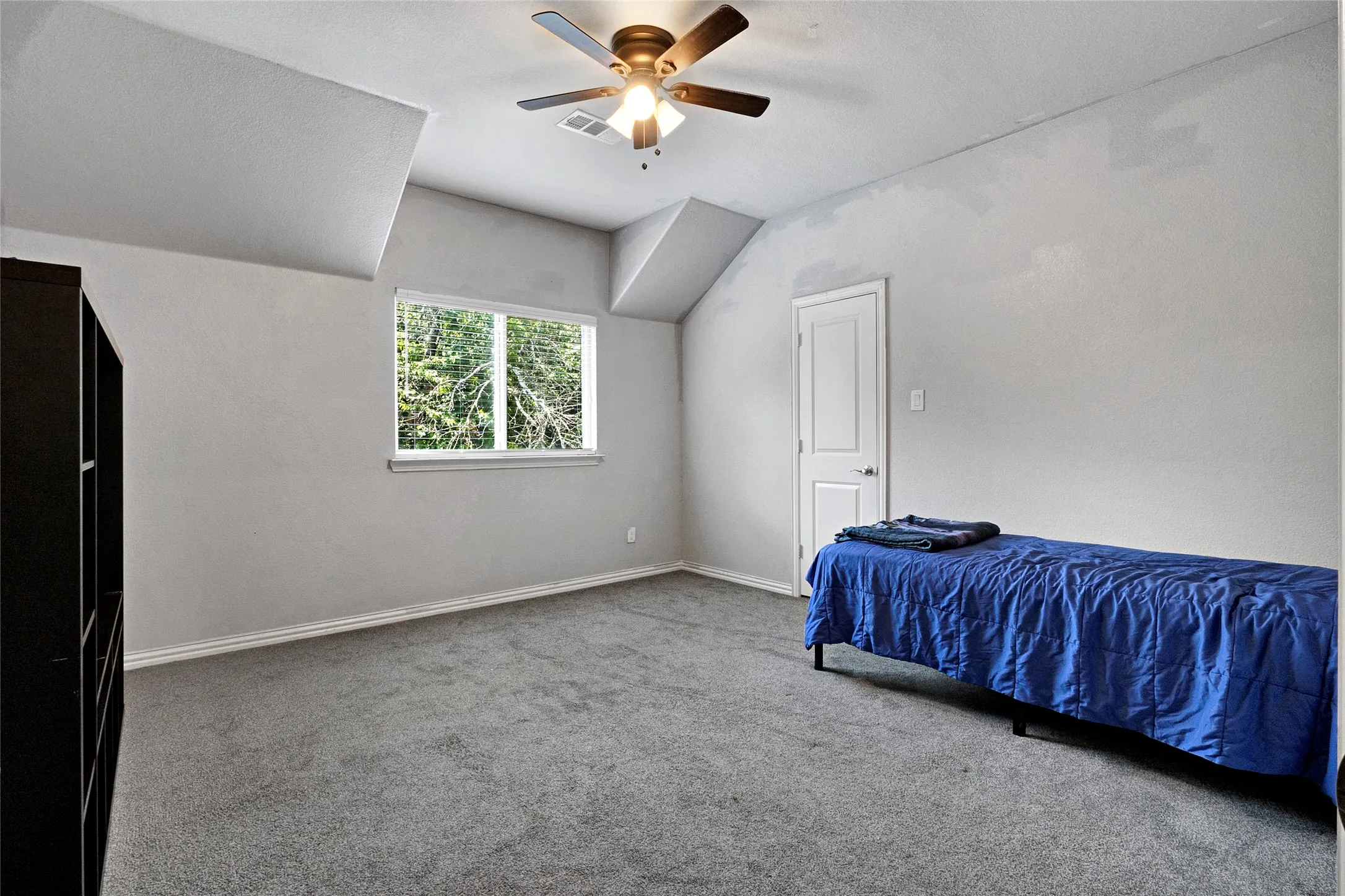 Carpeted room with a ceiling fan, a window overlooking trees, white baseboards, and a white door