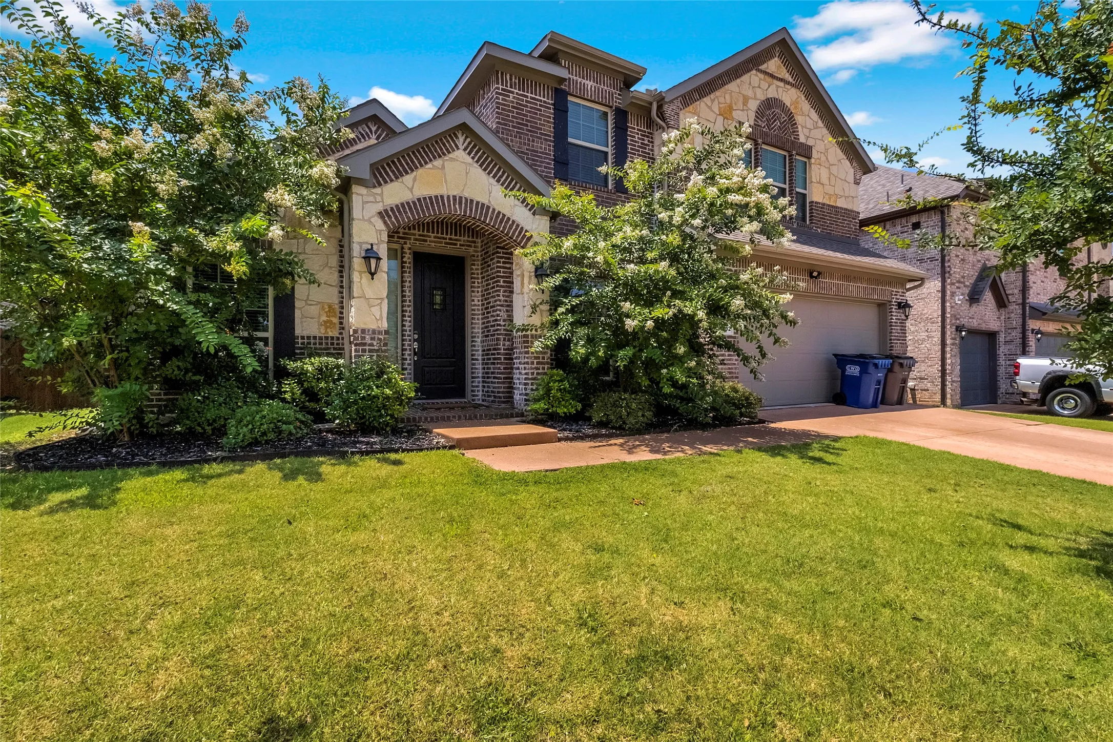 Two-story residence featuring a brick and stone facade, arched entryway, attached garage, manicured lawn, and mature landscaping