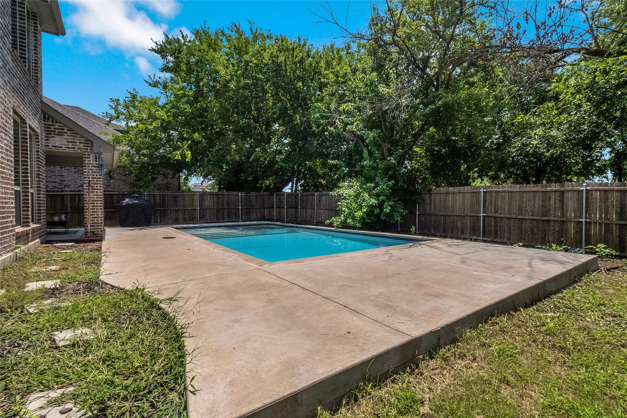 Private backyard oasis featuring a rectangular swimming pool with integrated concrete patio surround, mature perimeter trees, and a privacy fence
