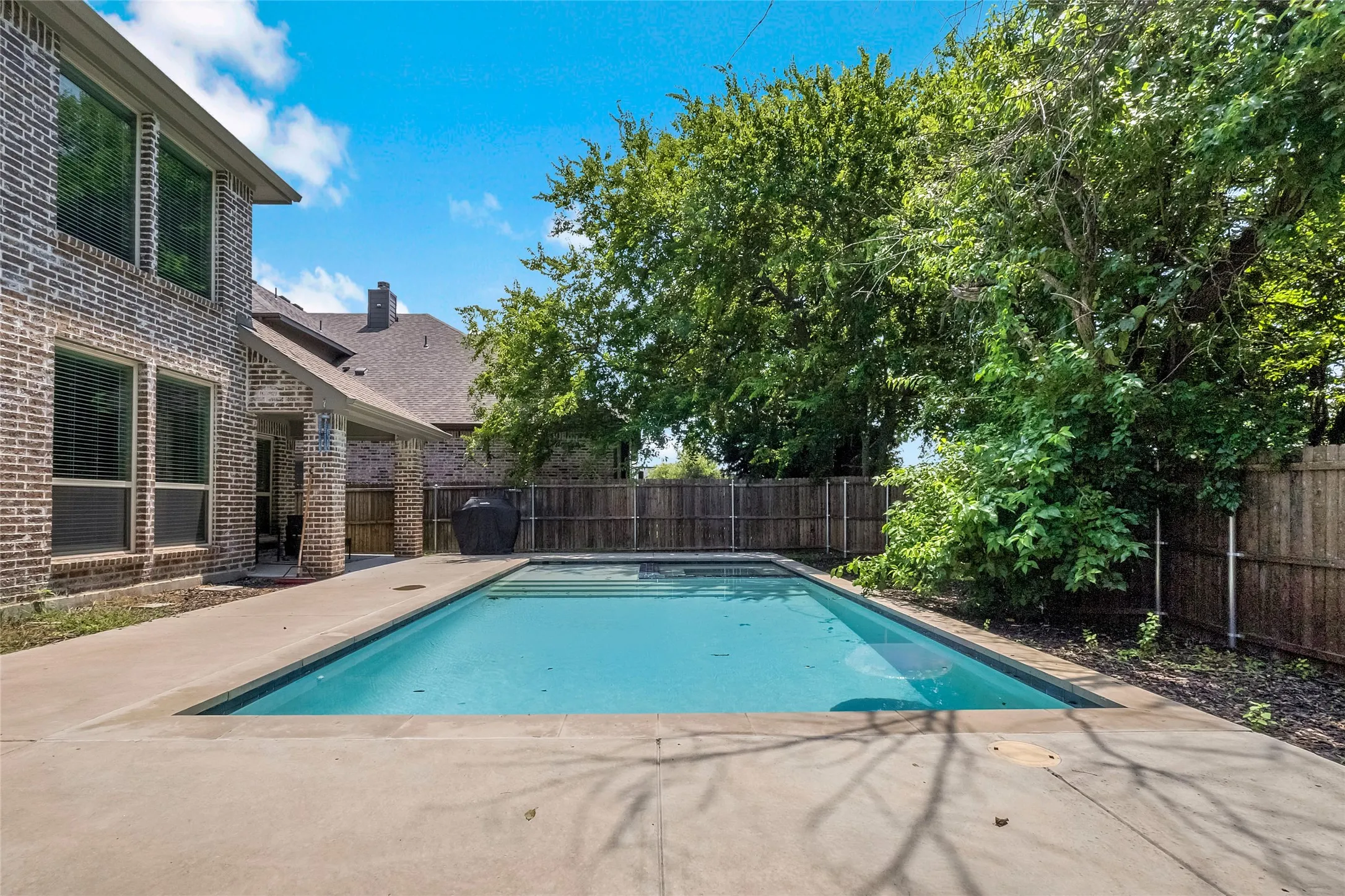 Backyard swimming pool with a concrete surround, surrounded by a wood privacy fence