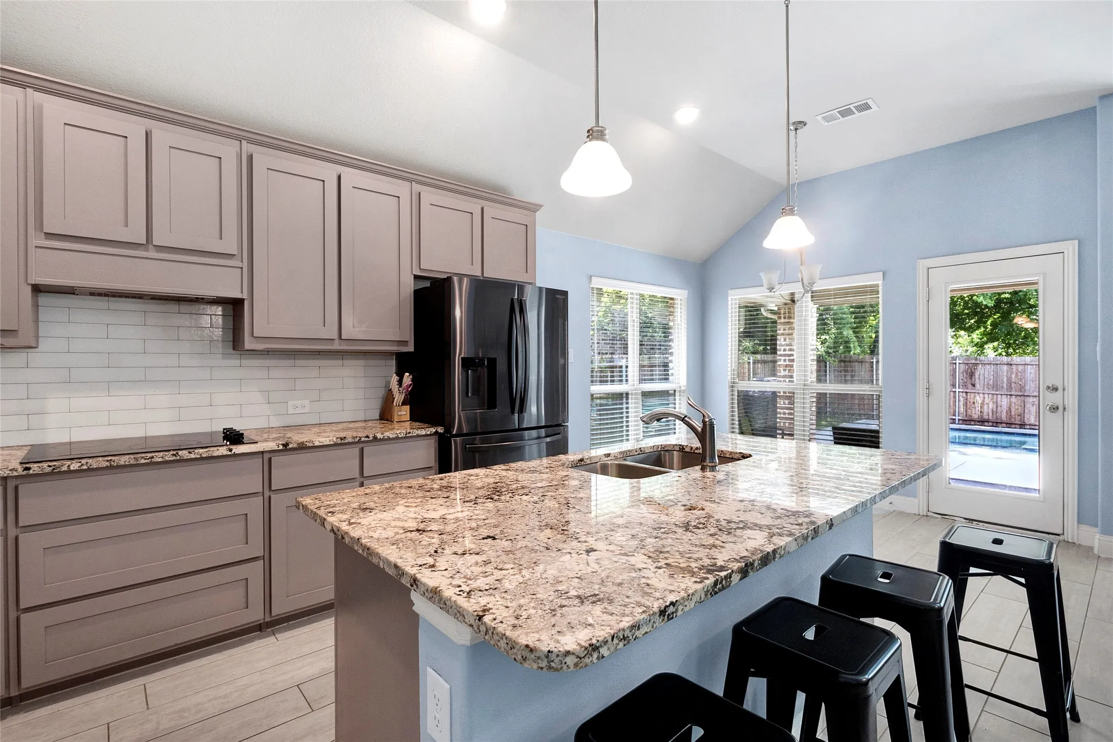 Open-concept kitchen featuring an expansive island with a double sink, black appliances, light-toned cabinetry, and subway tile backsplash