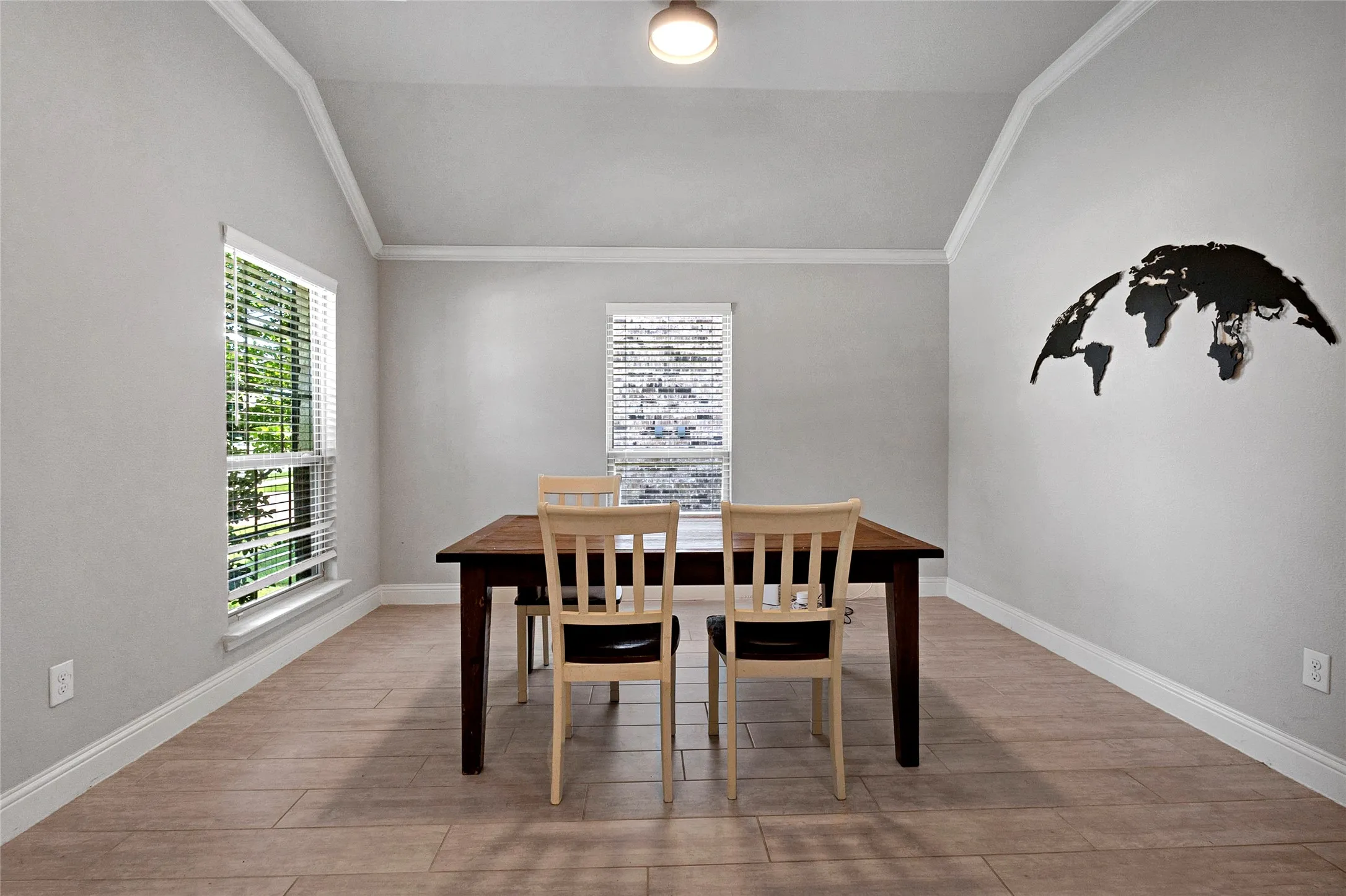 Vaulted ceilings with crown molding accent this space featuring wood-finish tile flooring and dual windows with blinds