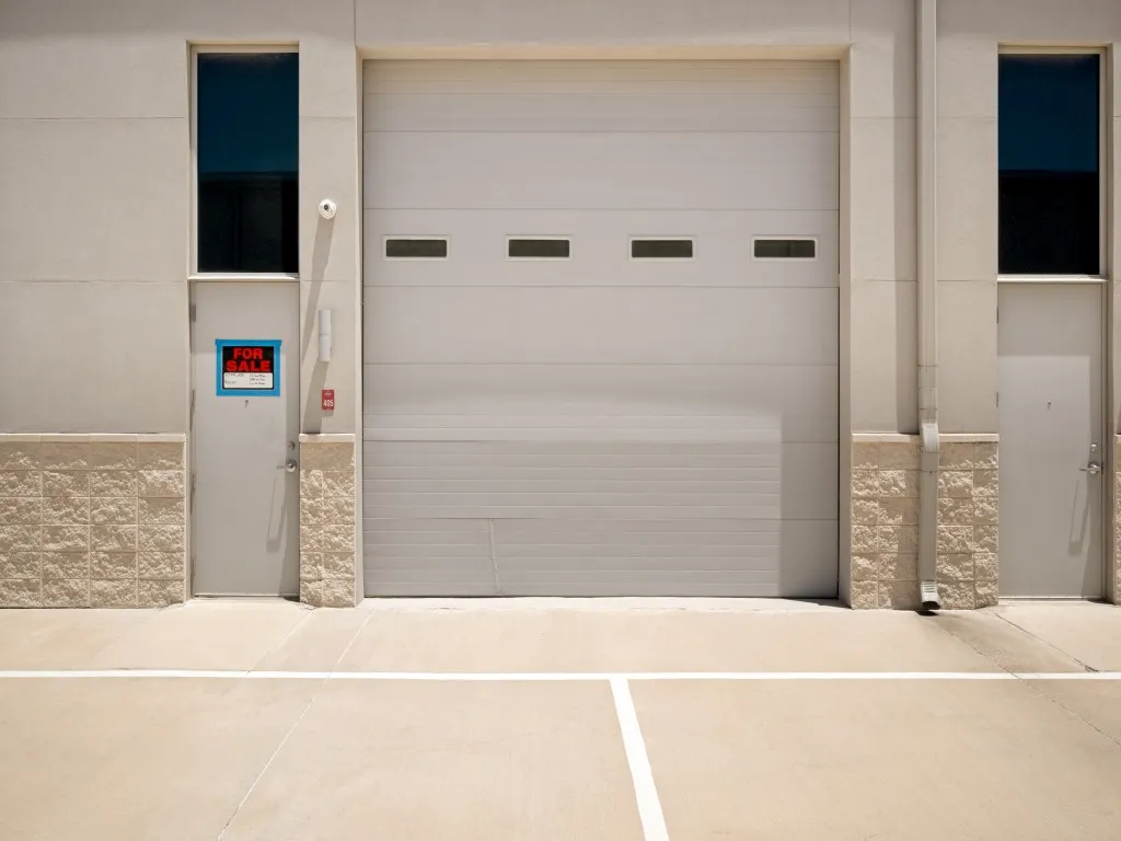 Commercial exterior featuring a large roll-up door with frosted panels, two entry doors, and upper-level windows