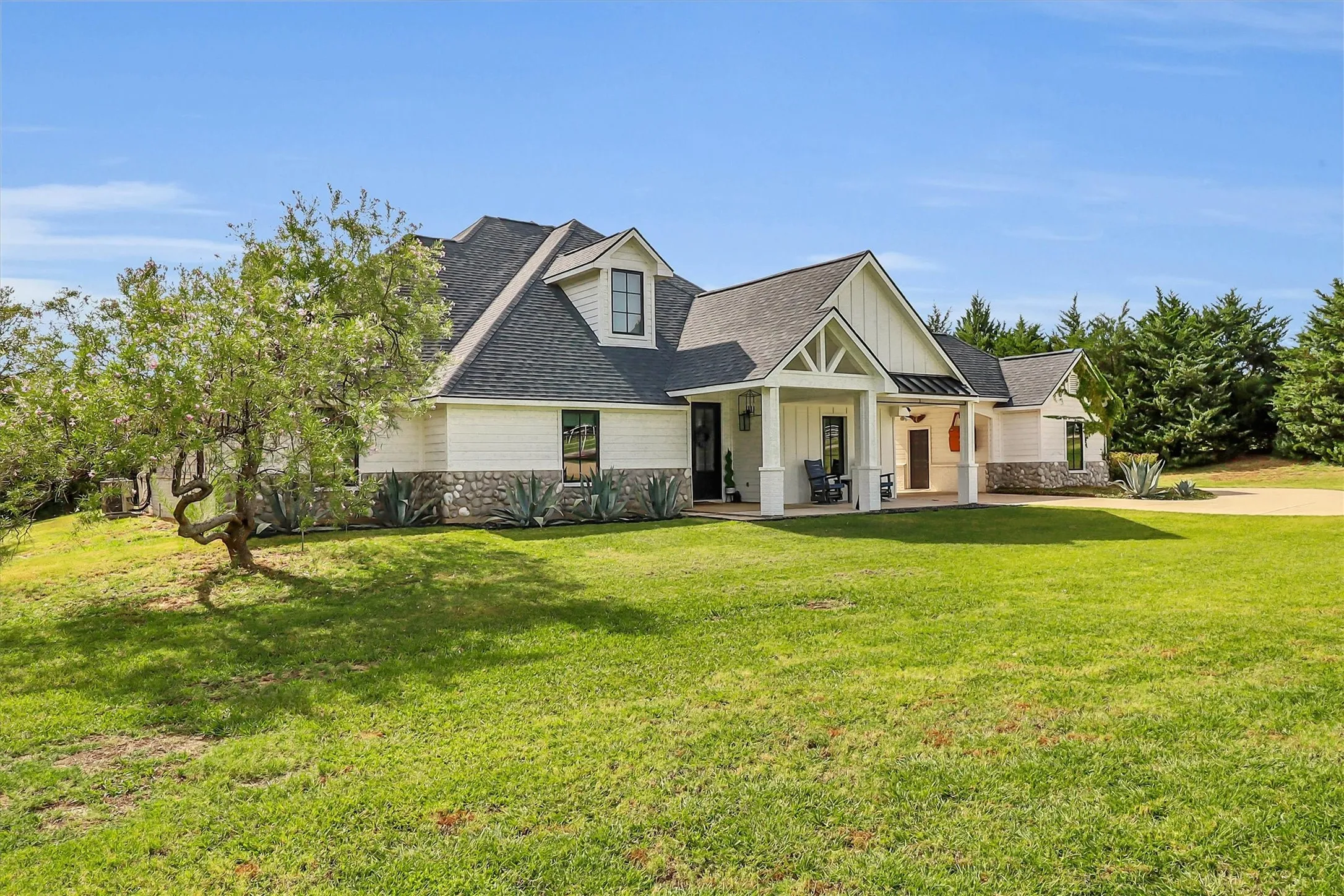 Modern farmhouse exterior with white siding, stone accents, and a dark roof