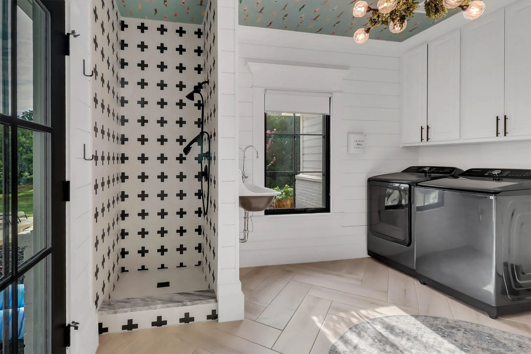 Utility room featuring a tiled shower stall with a black and white cross pattern, a built-in utility sink, and wood-finish herringbone flooring