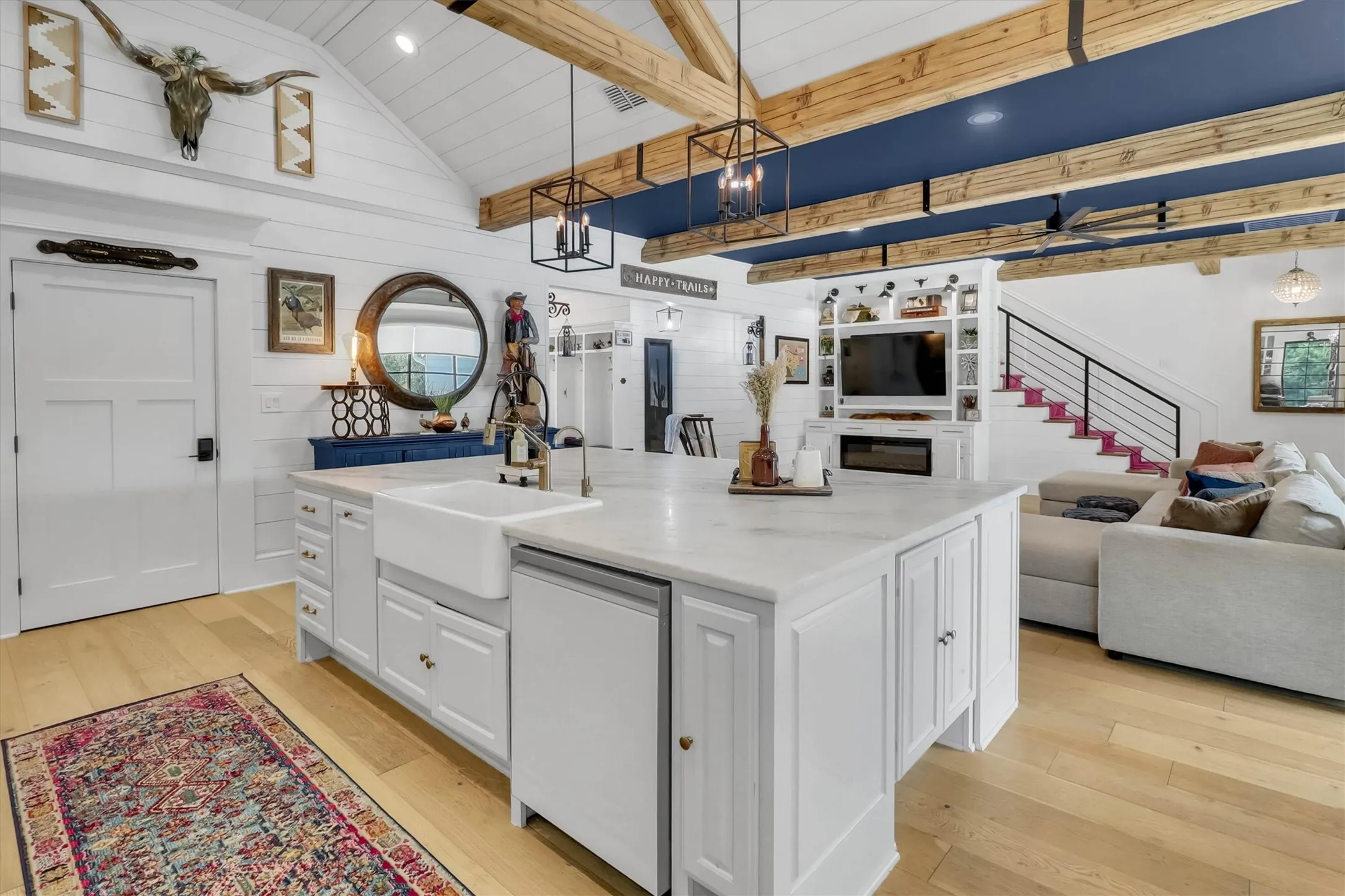 Spacious open-concept interior featuring light wood-finish flooring, a white vaulted ceiling with exposed wood beams, and shiplap wall finishes
