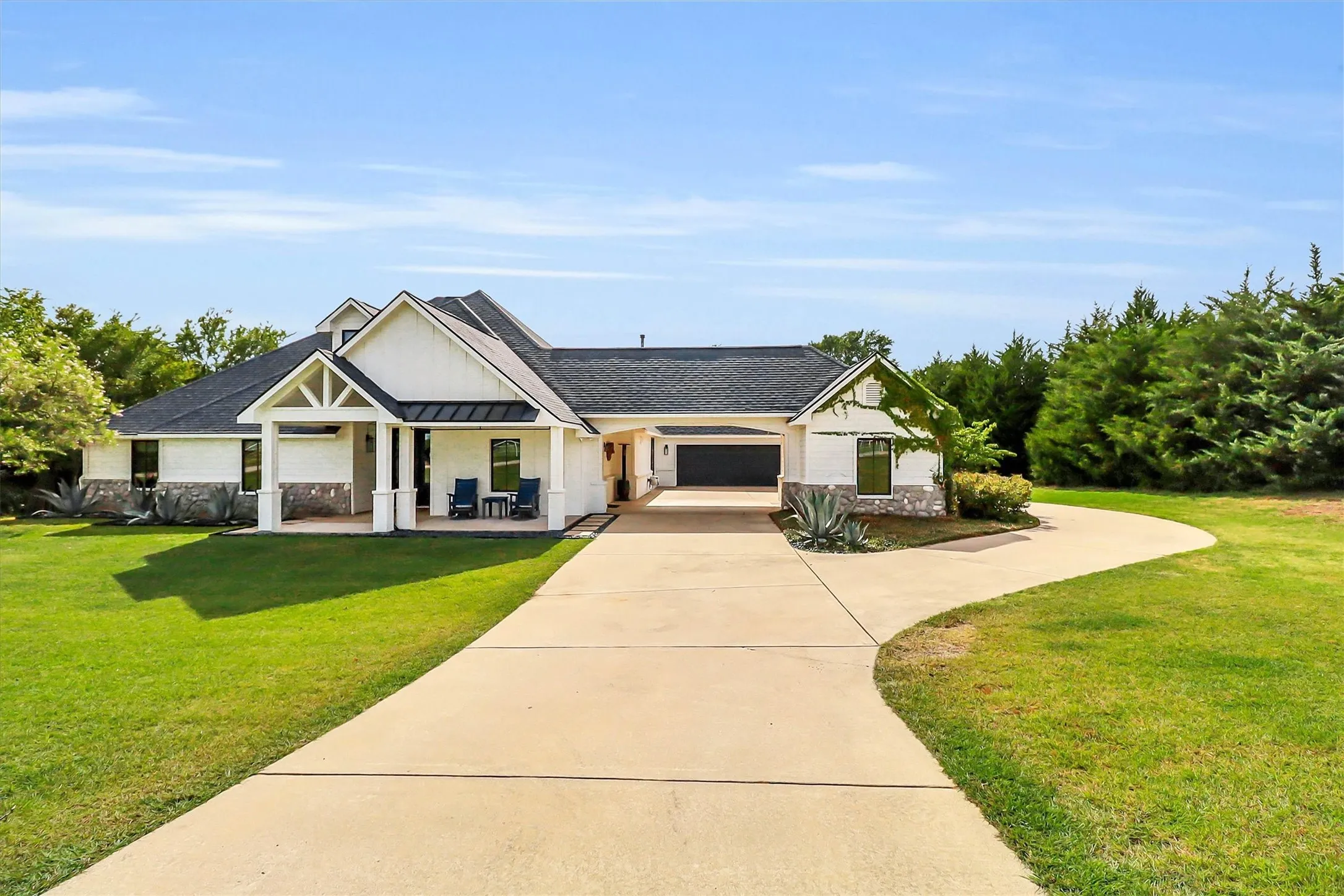 Contemporary exterior featuring white siding, stone accents, a dark shingle roof, and a covered front porch