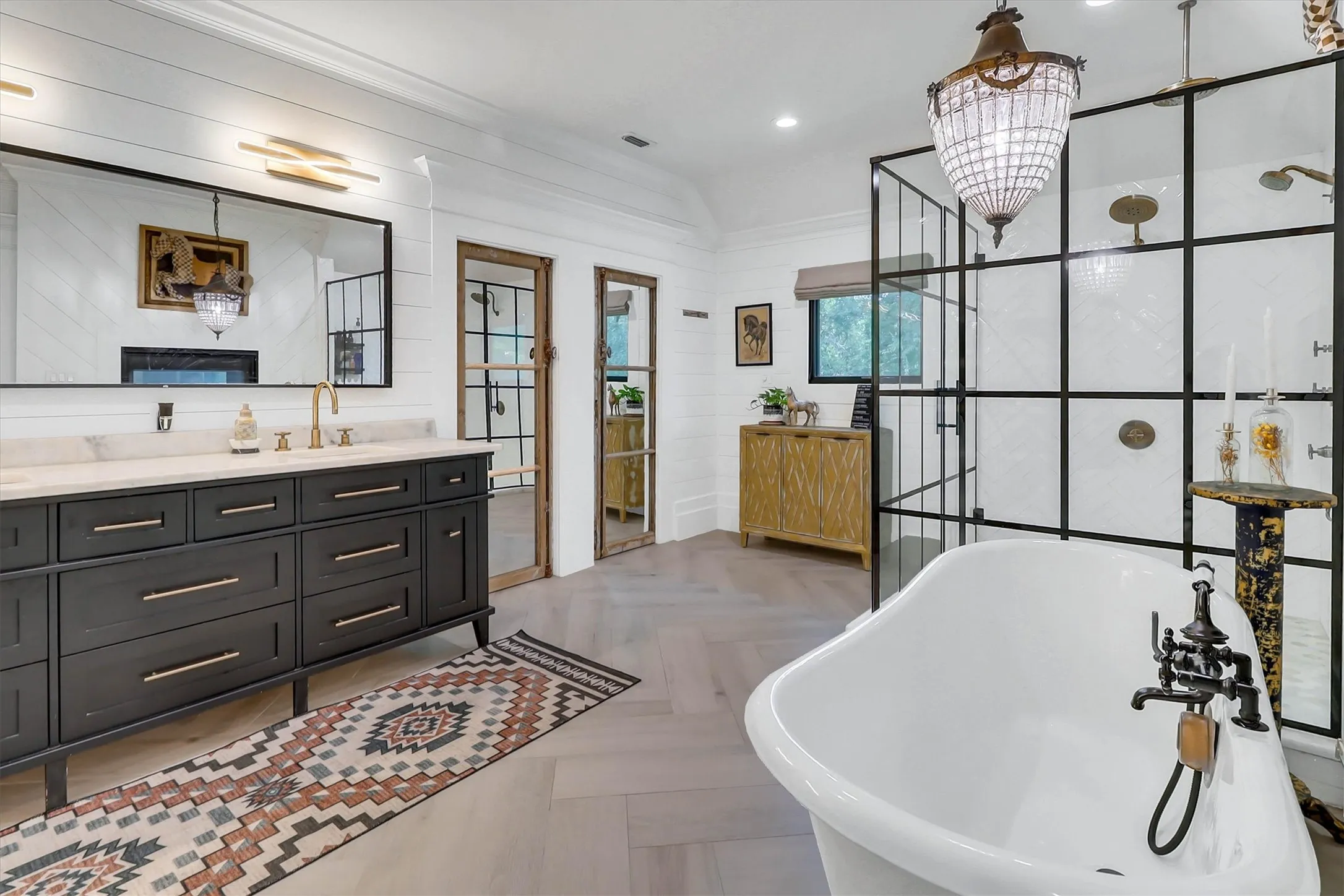Freestanding soaking tub with a dark bronze faucet, herringbone wood-finish flooring, and a walk-in shower with grid-patterned glass enclosure
