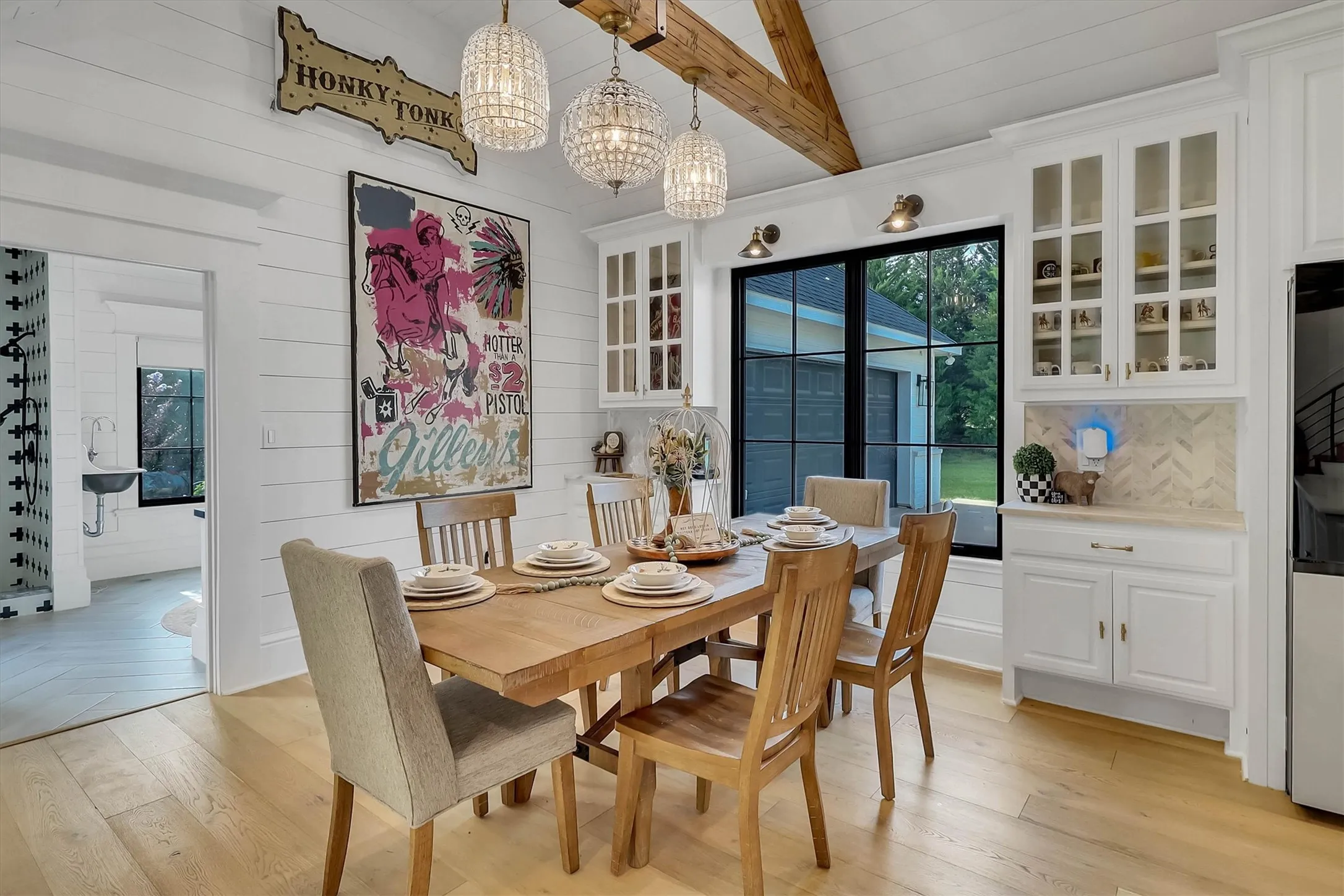 Bright dining area featuring wood-finish flooring, white shiplap walls, and a vaulted ceiling with exposed wood beams