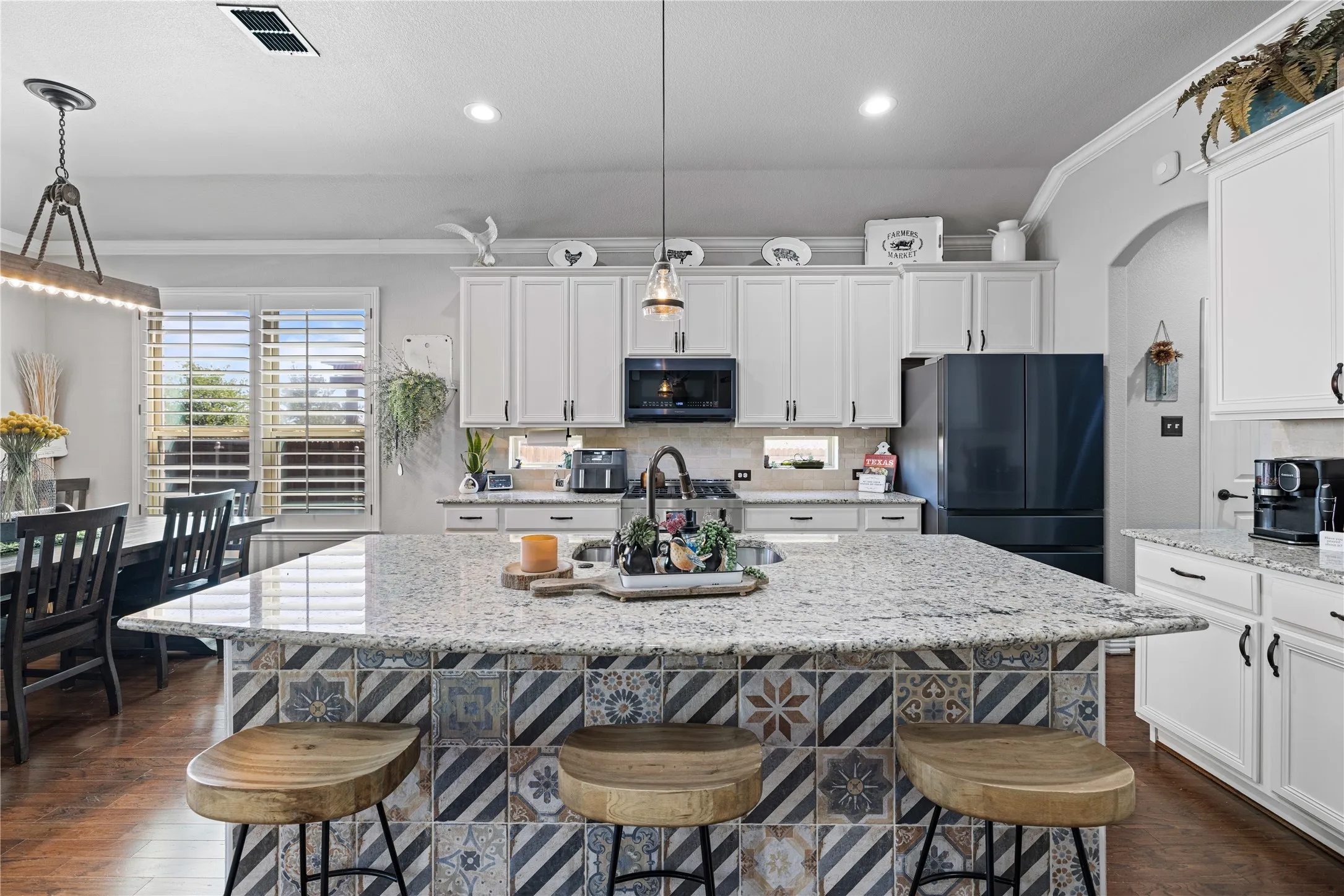 Kitchen with dark wood-type flooring, decorative light fixtures, black fridge, and a center island with sink