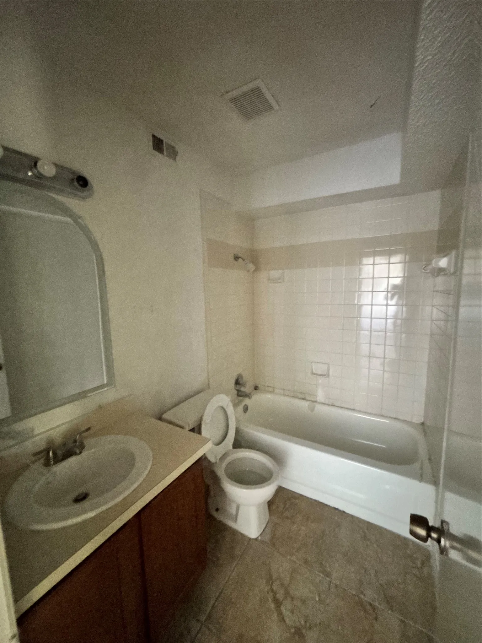 Bathroom featuring a wood-finish vanity with an integrated sink, a rectangular mirror, a white bathtub, and white square wall tiles
