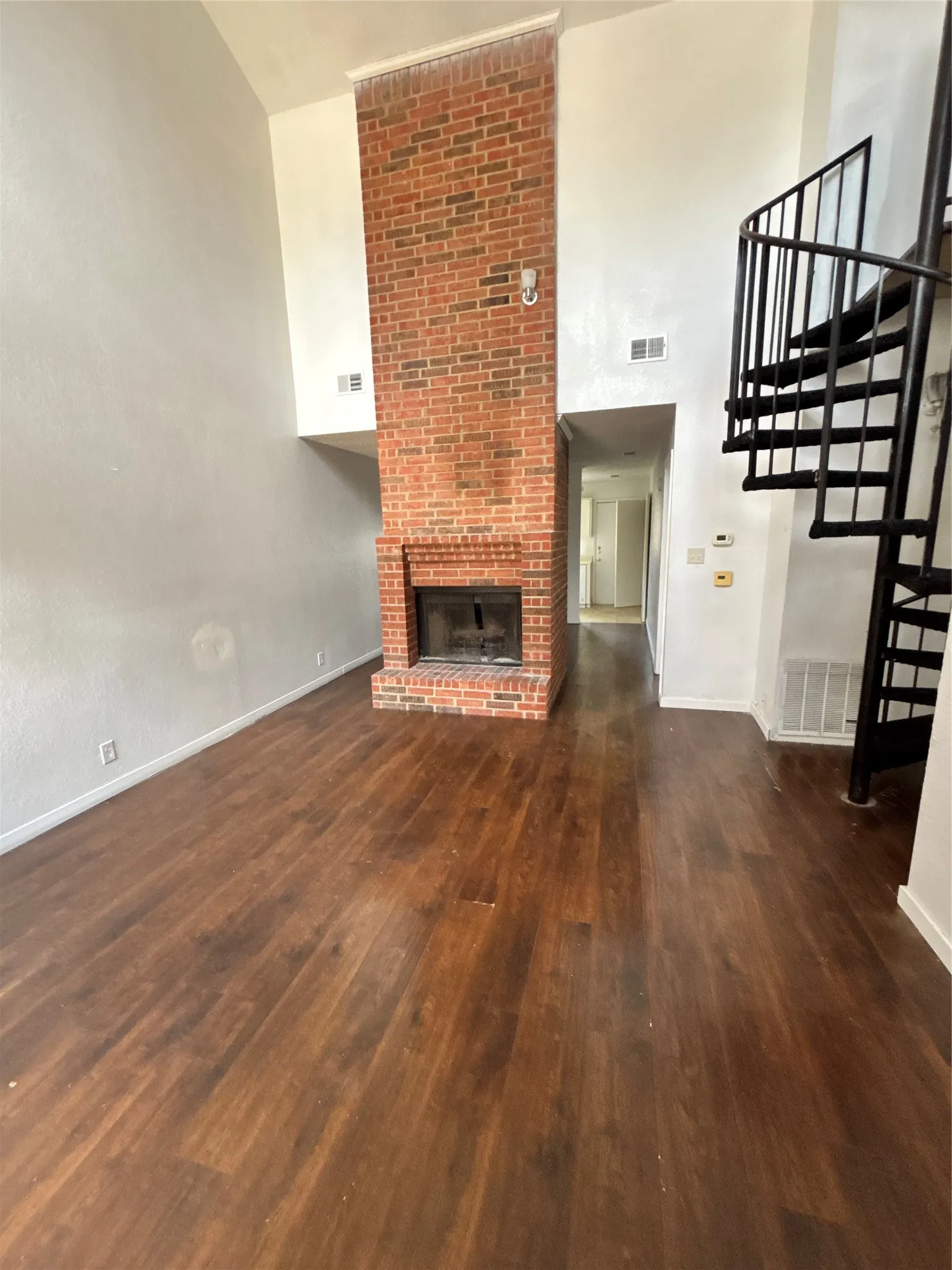 Living area featuring vaulted ceilings, a brick fireplace, dark wood-finish flooring, and a black spiral staircase