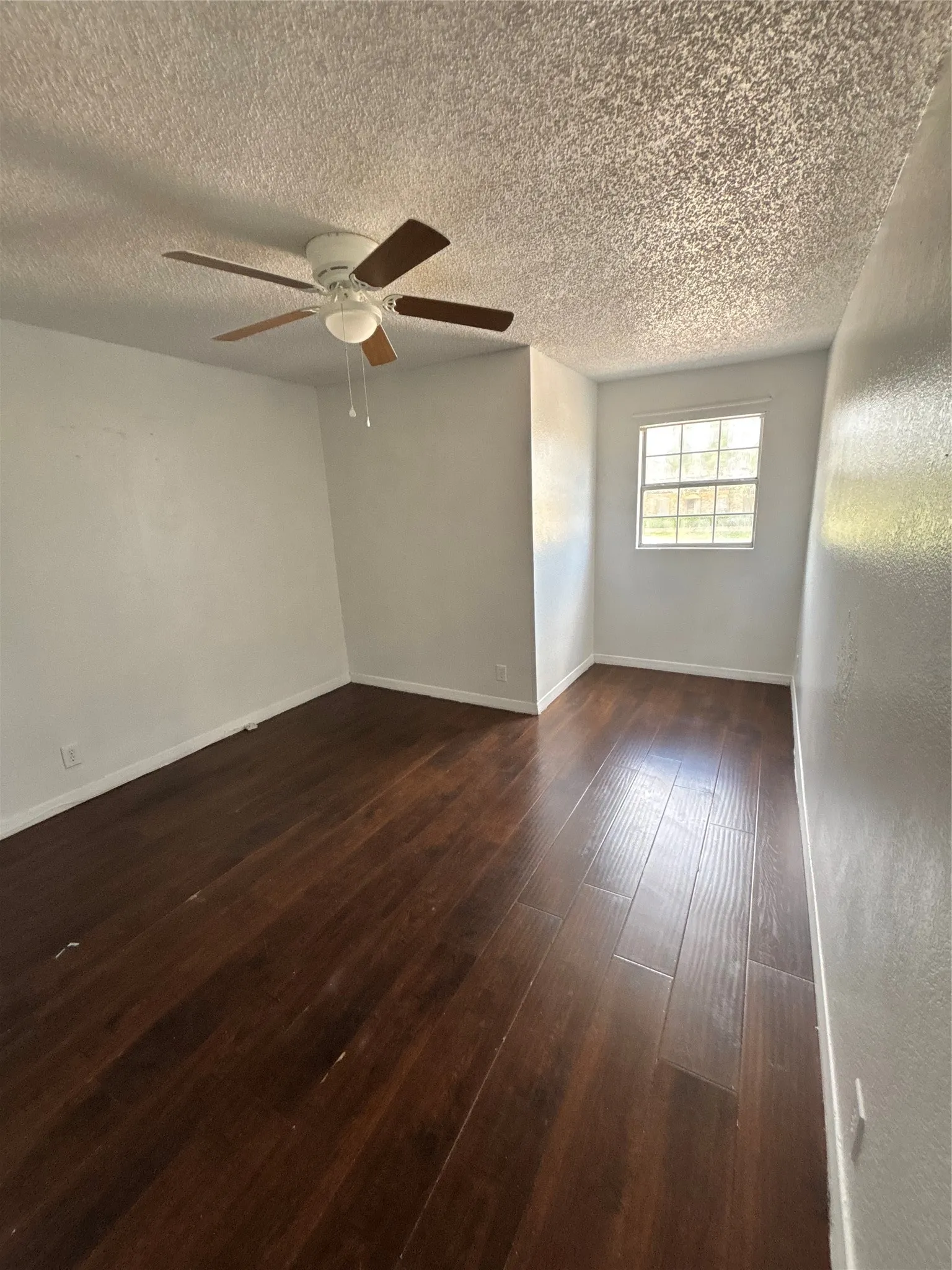Spacious room featuring wood-finish flooring, a ceiling fan with light fixture, and a window providing natural illumination