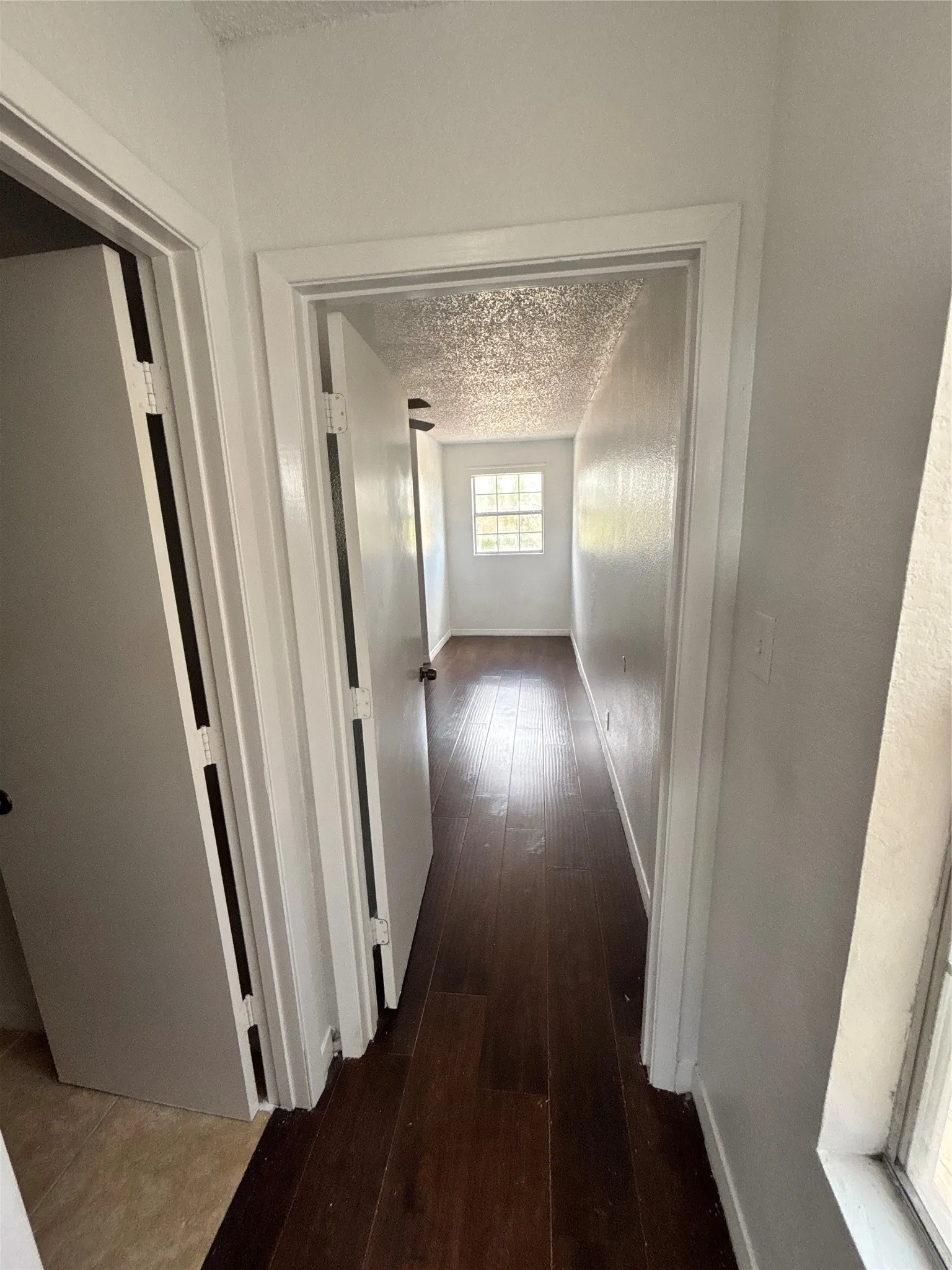 Hallway featuring dark wood-finish flooring, white painted walls, and a window providing natural light