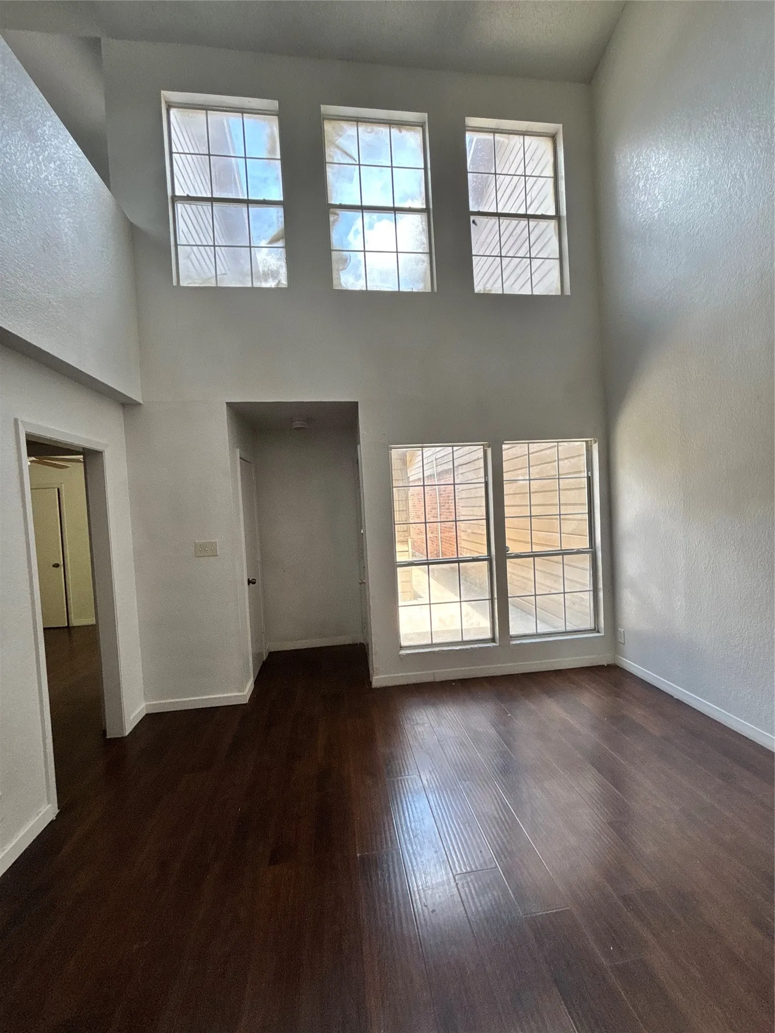 Two-story living area featuring dark wood-finish flooring and multiple windows