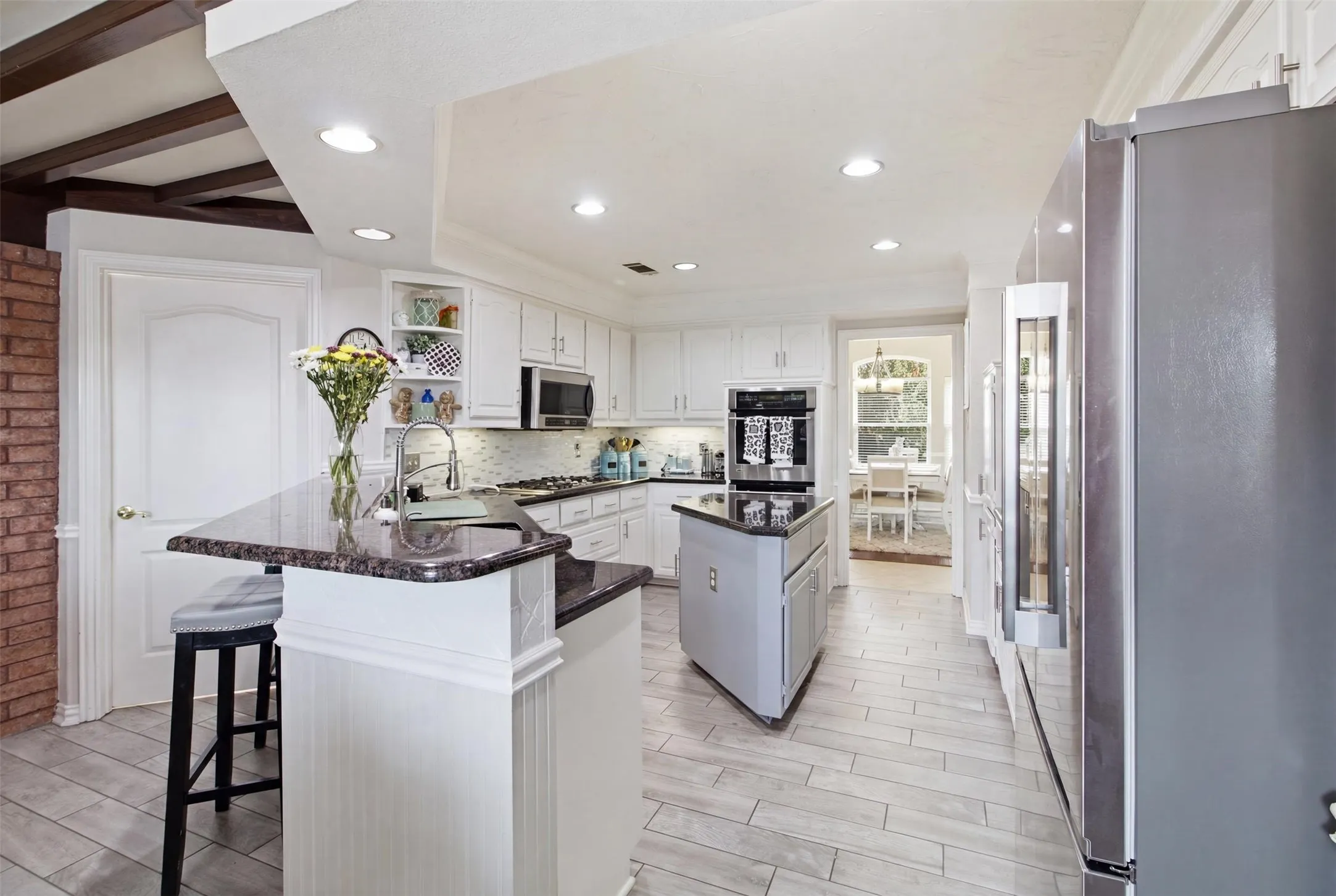 Kitchen featuring white cabinetry, dark stone countertops, wood-finish flooring, recessed lighting, and a kitchen island with a built-in sink
