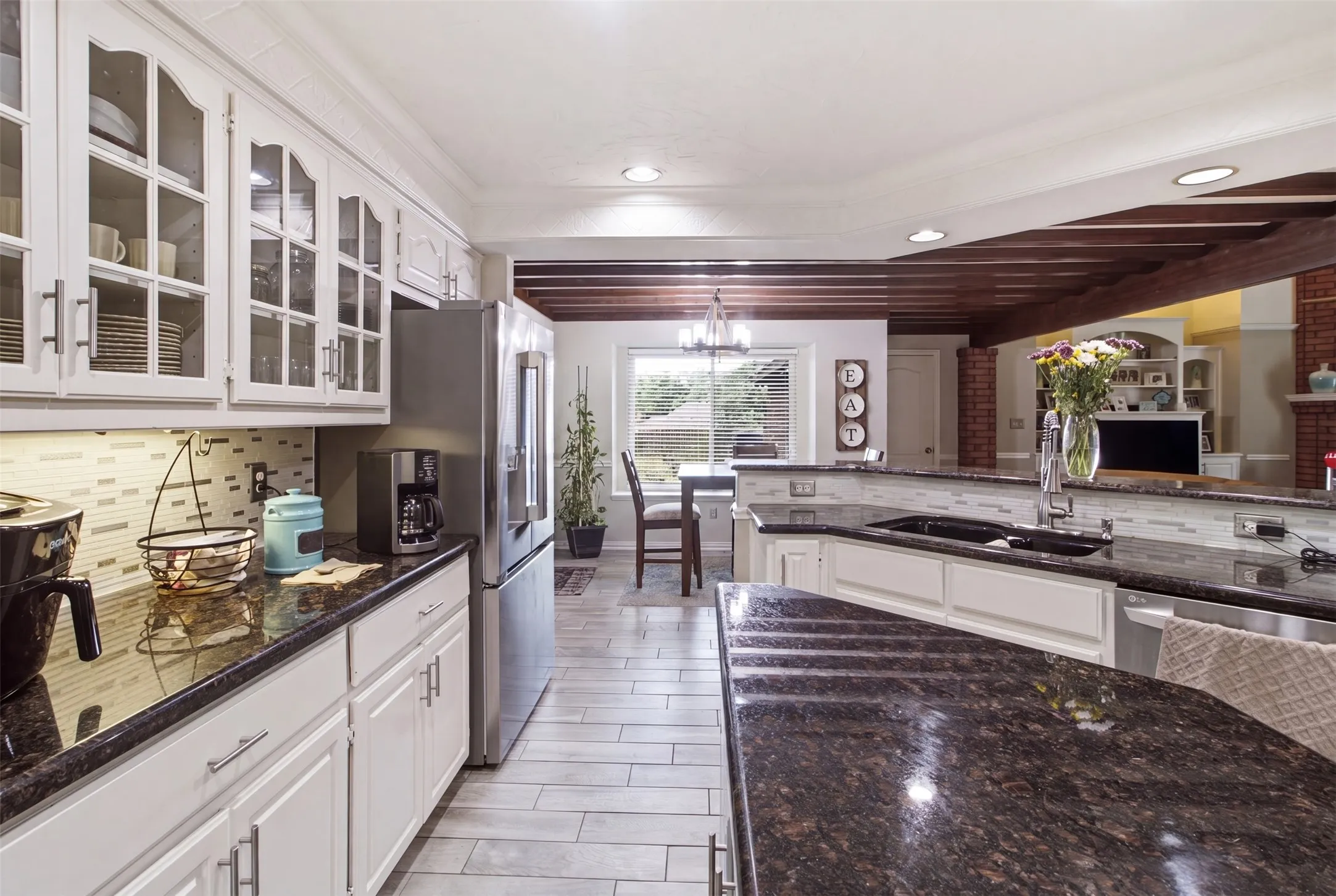 Open-concept kitchen featuring white cabinetry, dark granite countertops, stainless steel appliances, and wood-look tile flooring