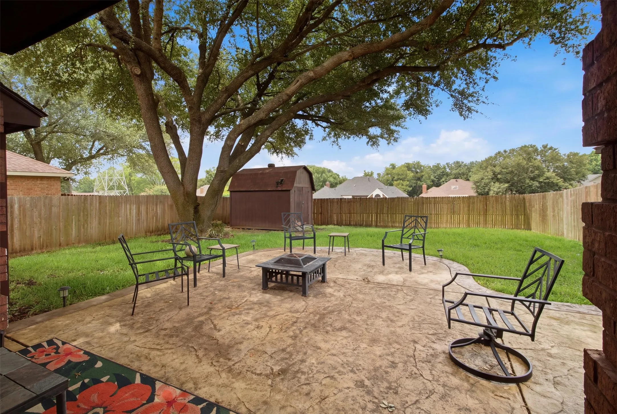 Expansive backyard featuring a stamped concrete patio, mature shade tree, manicured lawn, wood privacy fencing, and an outdoor storage shed
