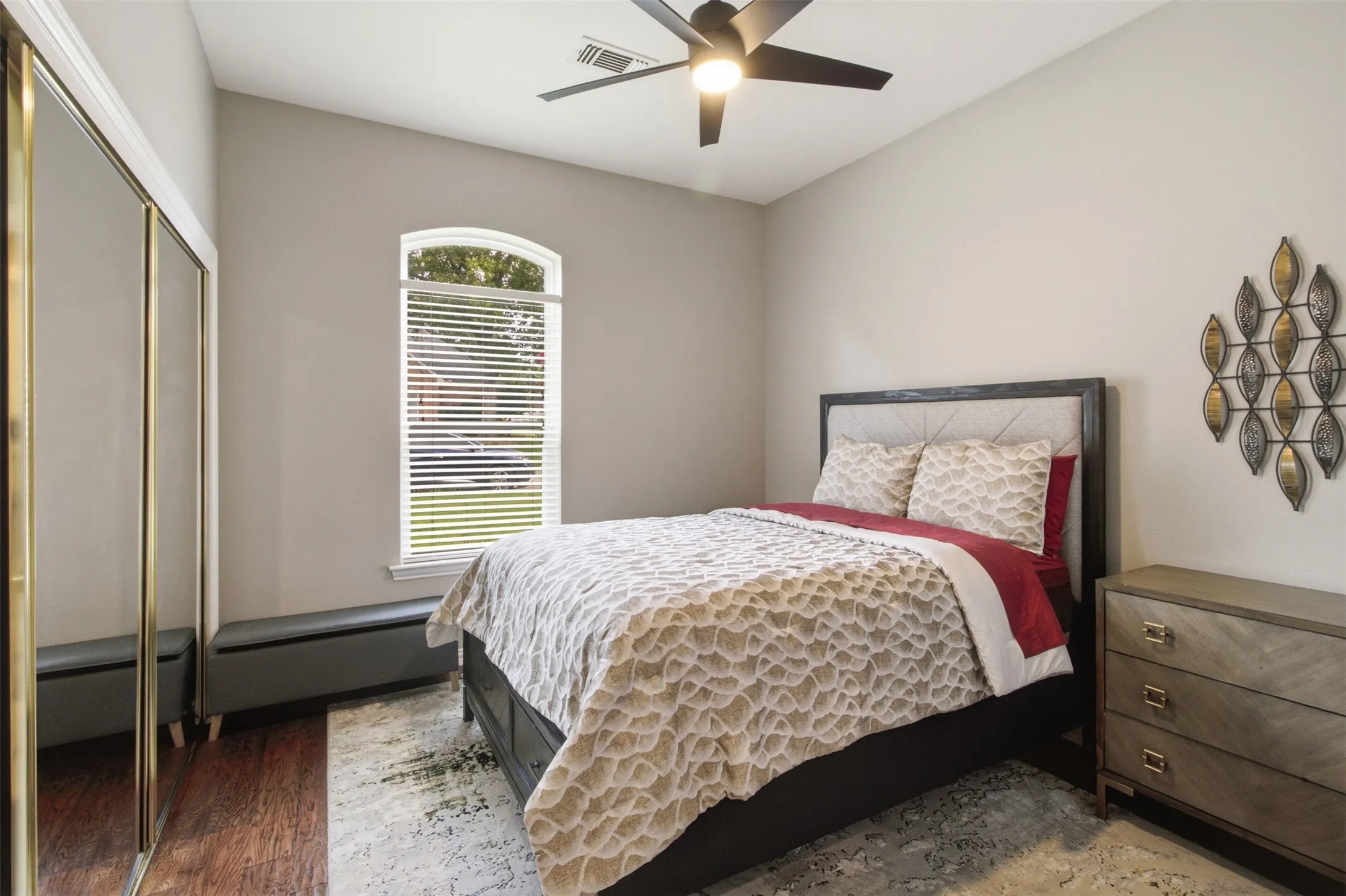 Bedroom featuring wood-finish flooring, an arched window with blinds, a ceiling fan with integrated lighting, and mirrored closet doors