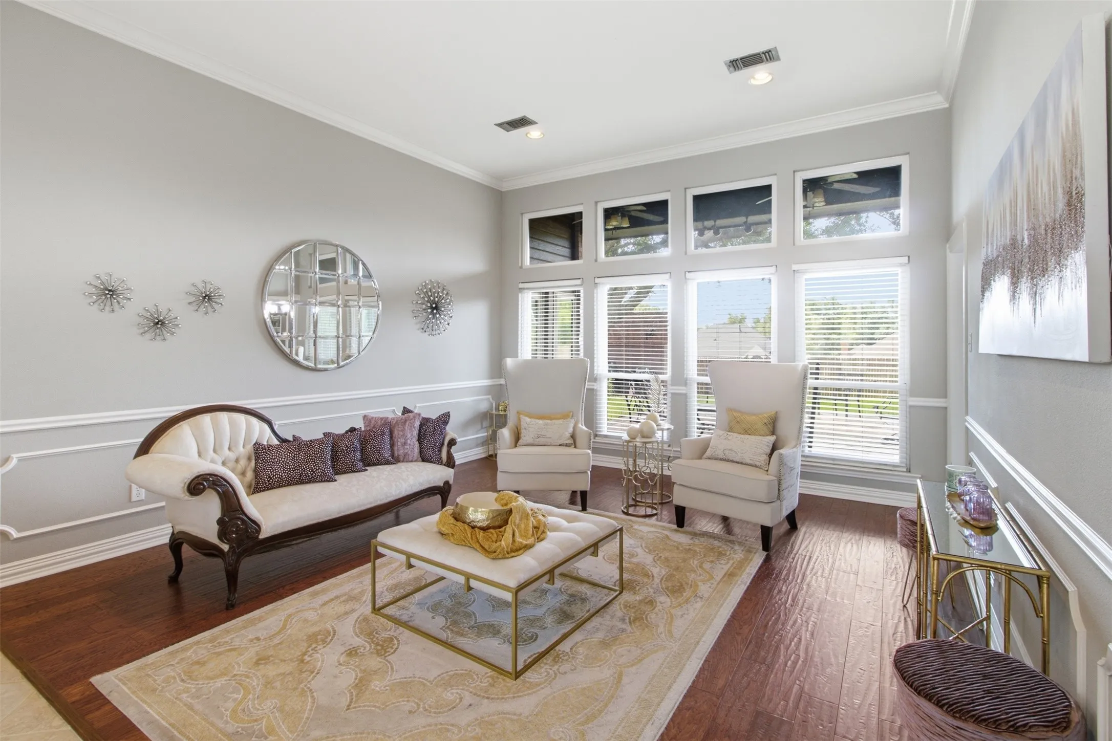 Living area featuring wood-finish flooring, extensive crown molding, chair rail detailing, and a multi-pane window array