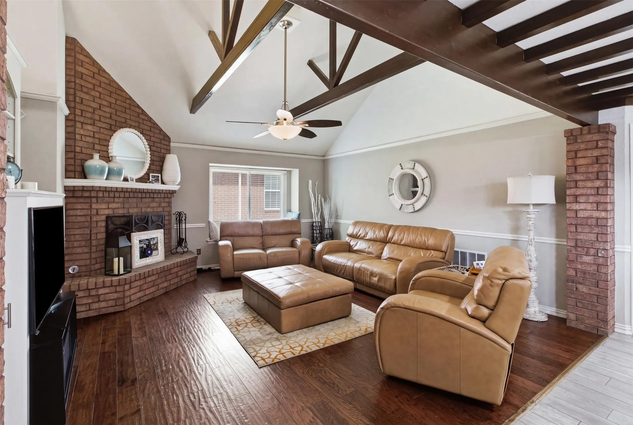 Living area featuring vaulted ceilings with exposed beams, a brick fireplace with a white mantel, and wood-finish flooring