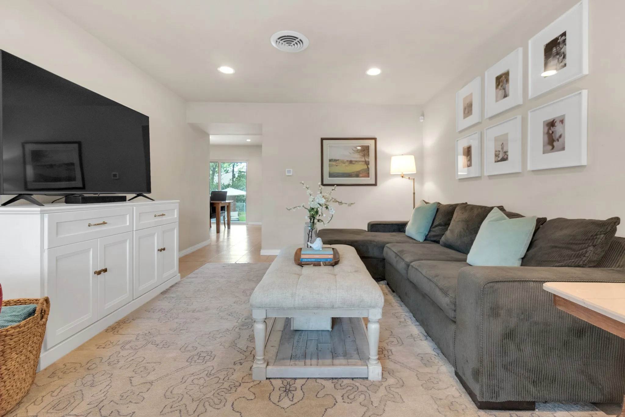 Recessed ceiling lighting illuminates a bright living space featuring light wall tones and a patterned area rug over wood-finish flooring