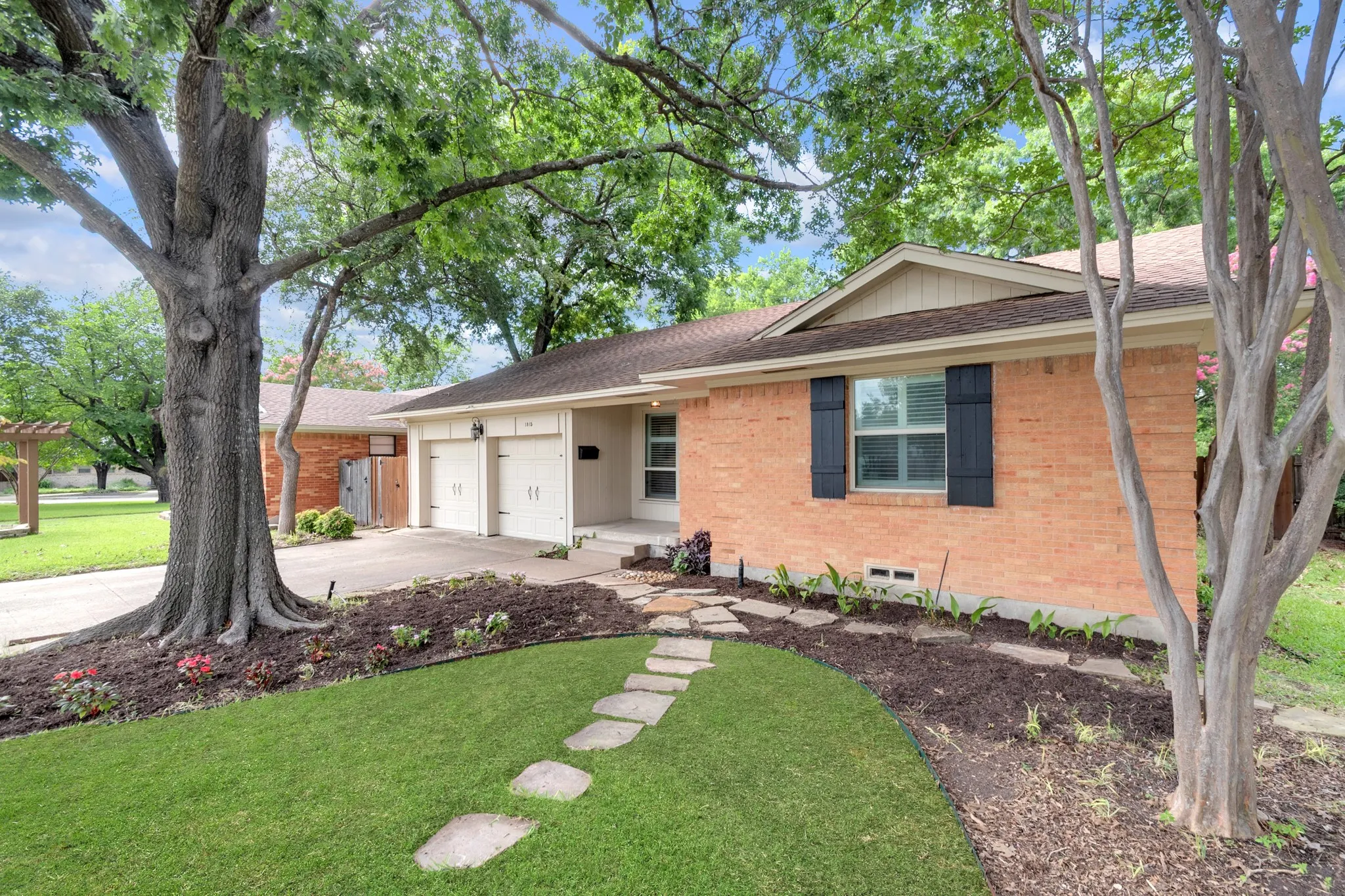Brick exterior with dark shutters, dual garage doors, and a stone pathway