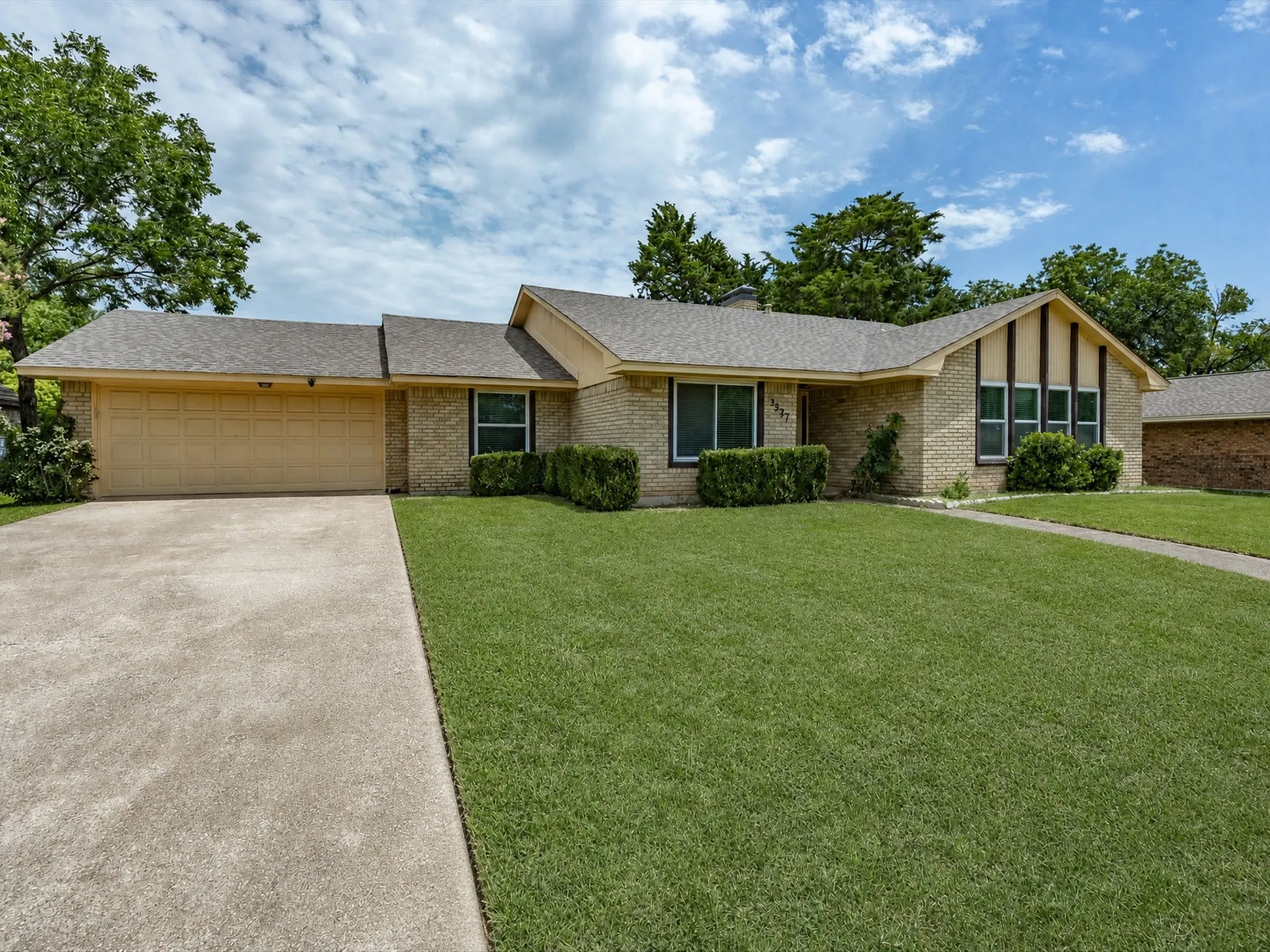 Brick exterior residence featuring a two-car garage, concrete driveway, and a front lawn with established landscaping