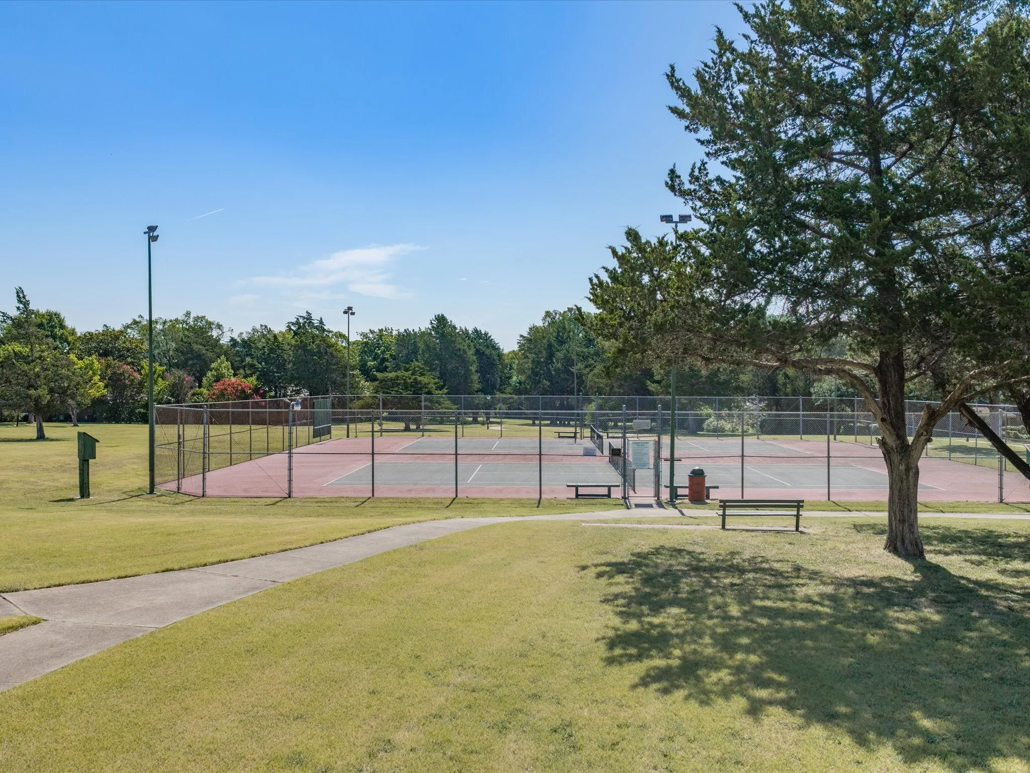 Outdoor tennis courts with chain-link fencing, surrounded by mature trees and manicured lawn